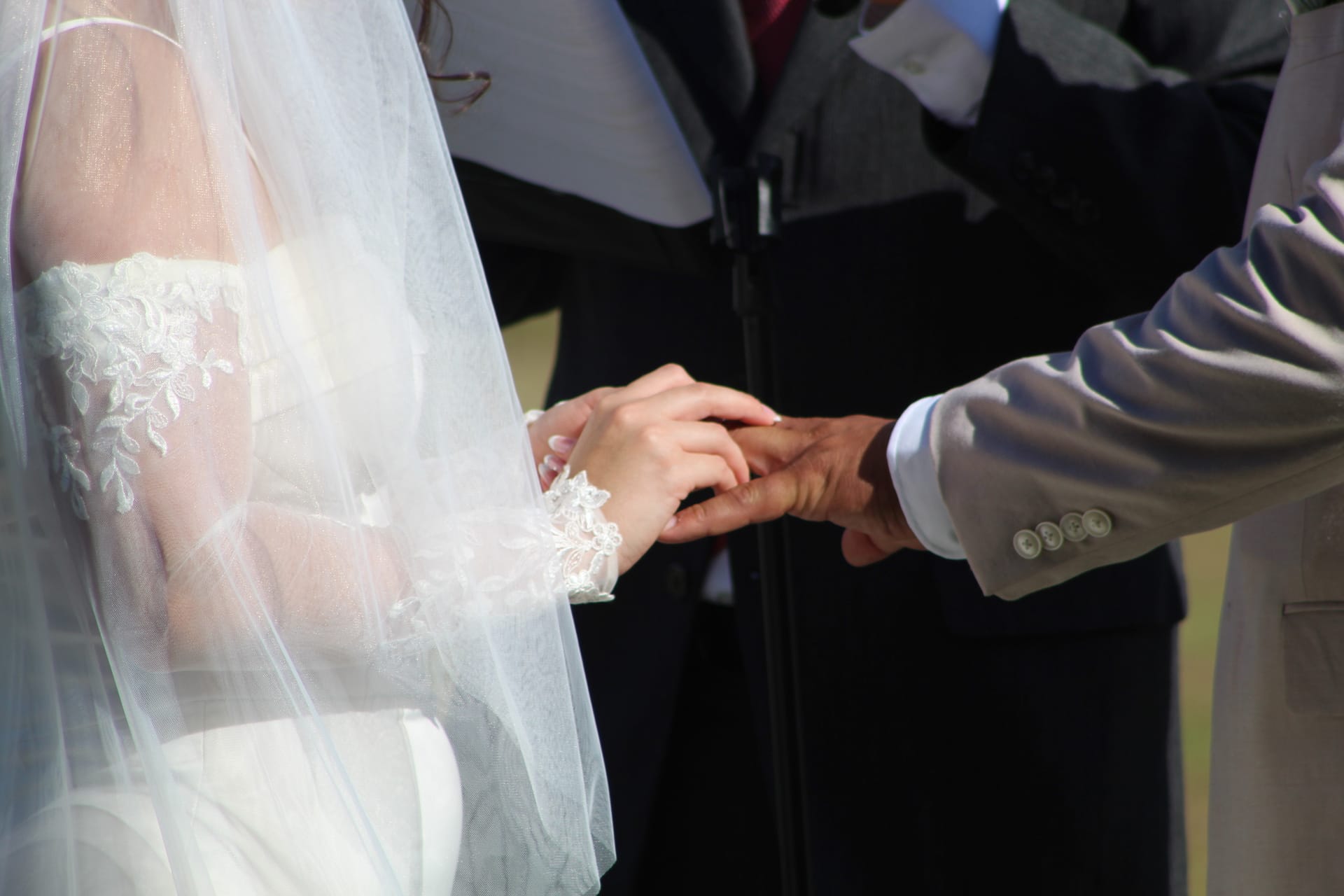 Groom placing a wedding ring on the bride's hand during the outdoor ceremony at Scarborough House, with delicate lace veil and bridal gown details visible.