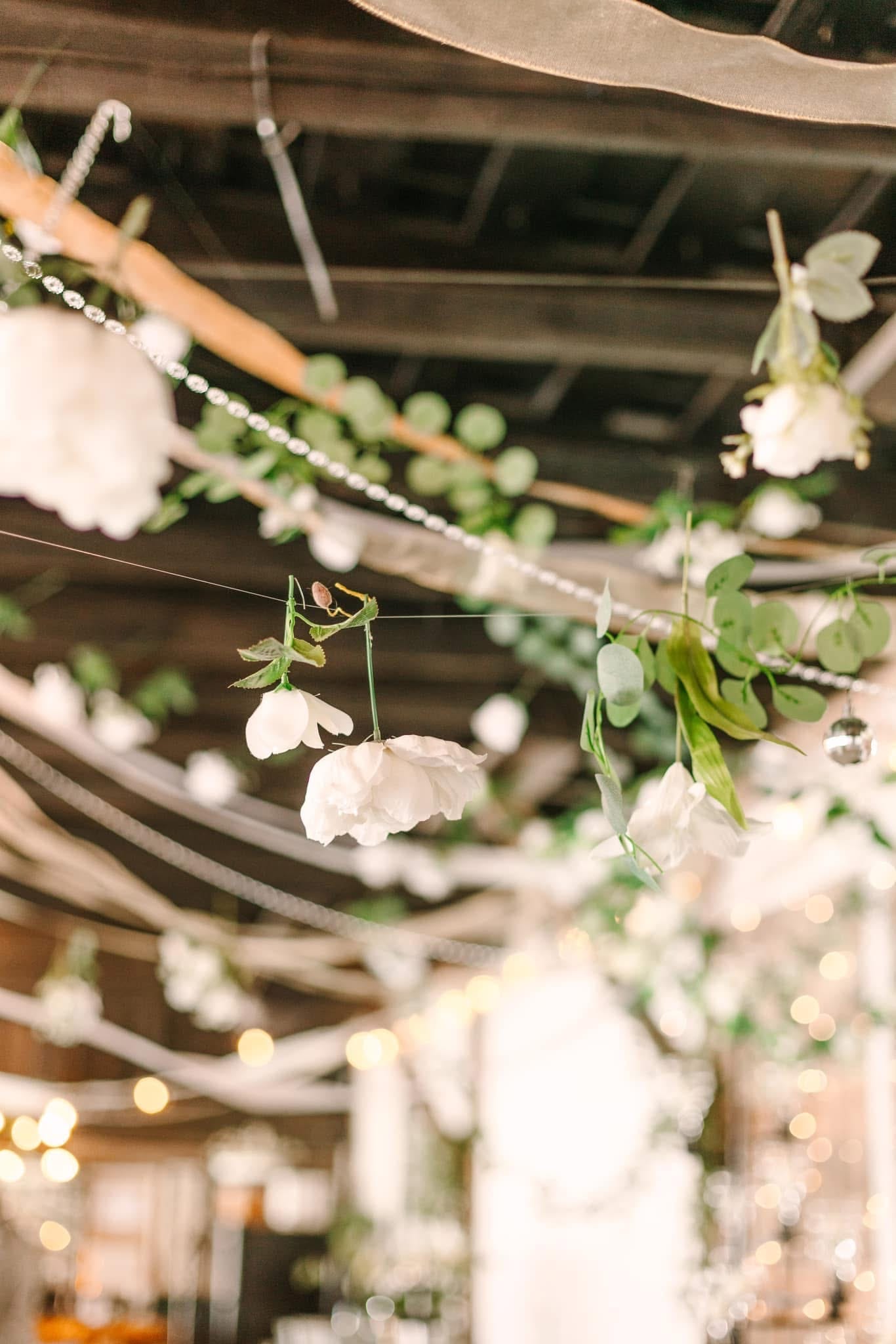 White blooms and lush greenery garlands draped across the ceiling of Scarborough House grand hall with soft warm bokeh lighting in the background.