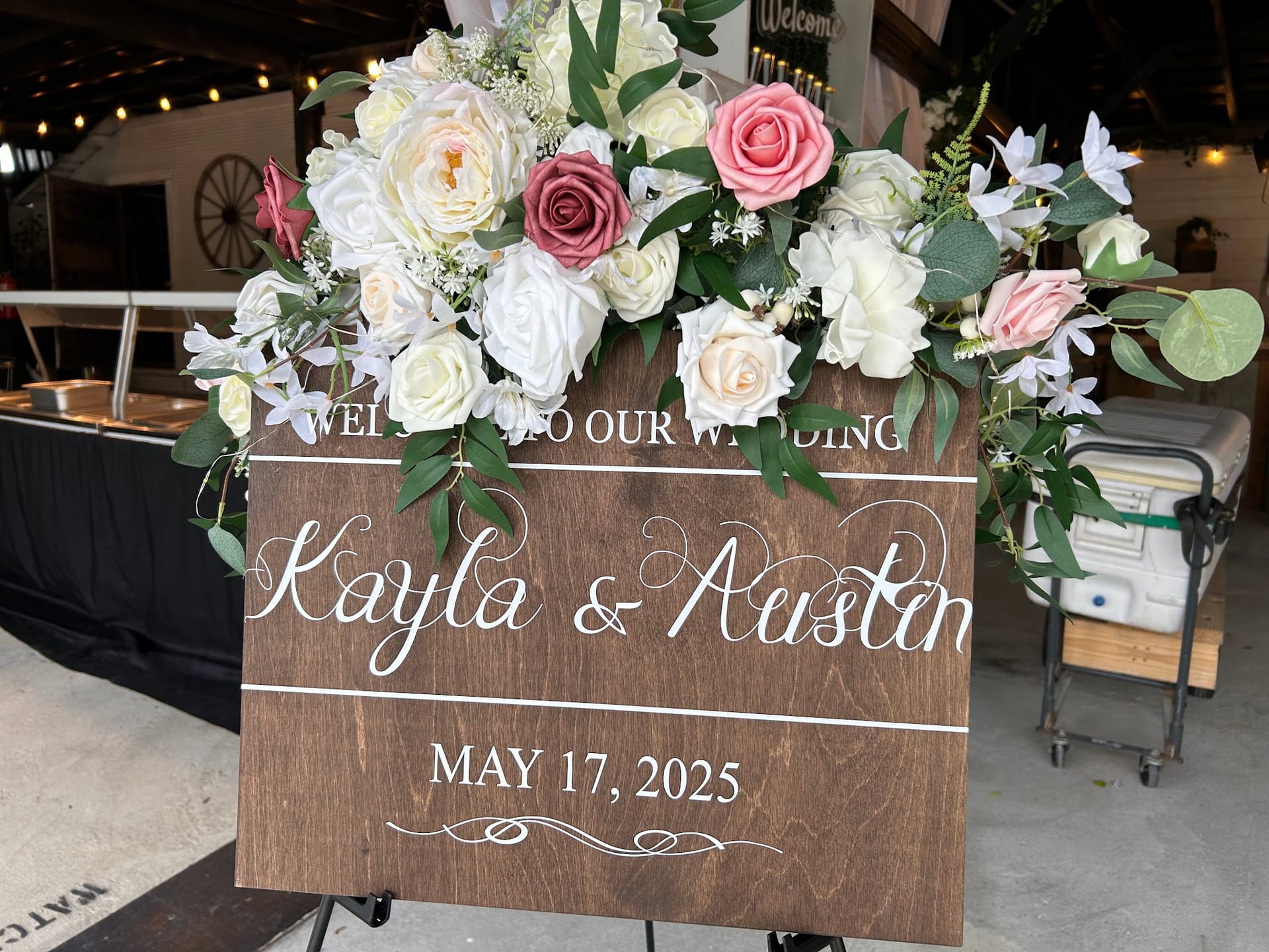 Rustic wooden wedding welcome sign for Kayla and Austin dated May 17 2025 adorned with white cream and dusty rose floral arrangement at Scarborough House.