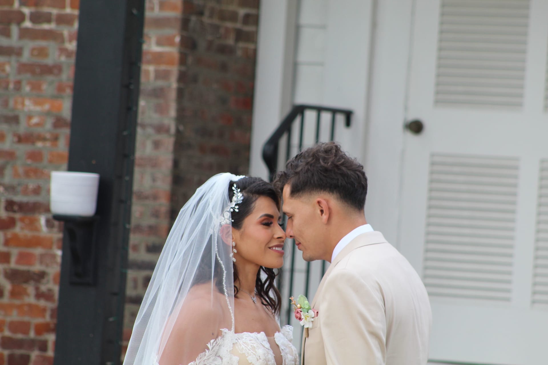 Bride in lace gown and veil touches foreheads with groom in cream suit outside the 1821 Scarborough House historic estate.