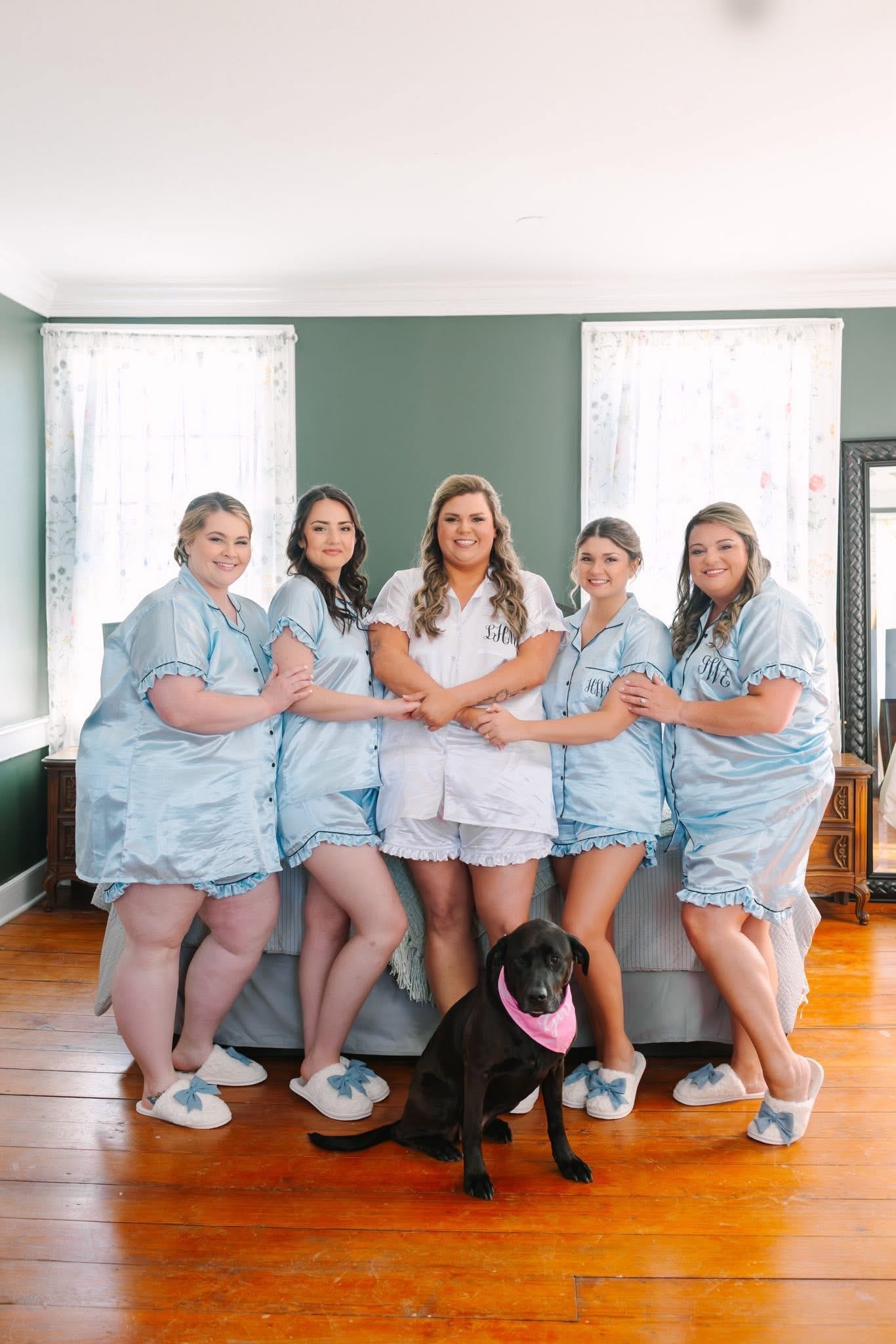 Bride in white monogrammed pajamas poses with four bridesmaids in light blue matching sets and a black Lab wearing a pink bandana inside a historic bridal suite at Scarborough House.
