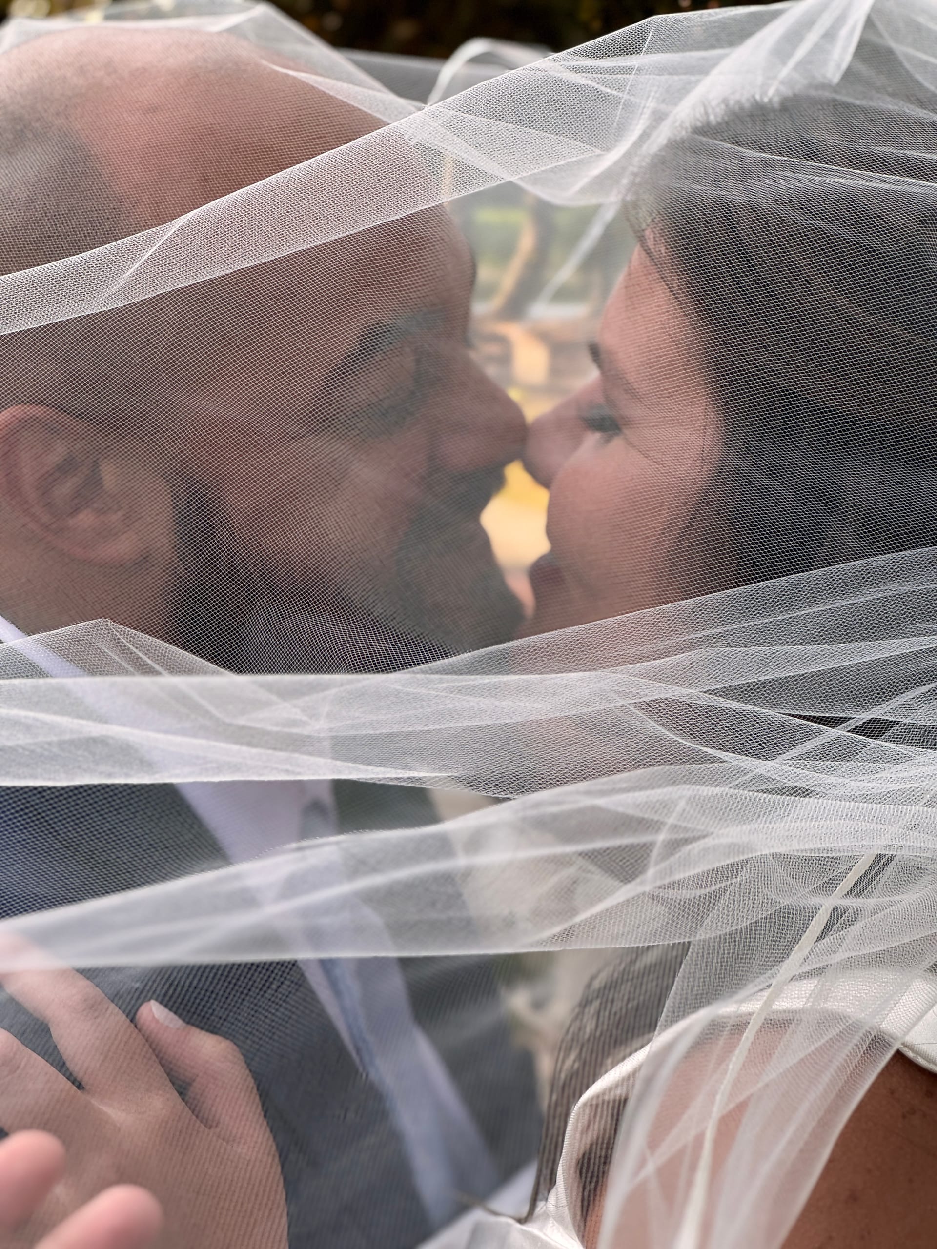 Bride and groom share an intimate near-kiss moment enveloped together beneath a flowing white bridal veil at Scarborough House.