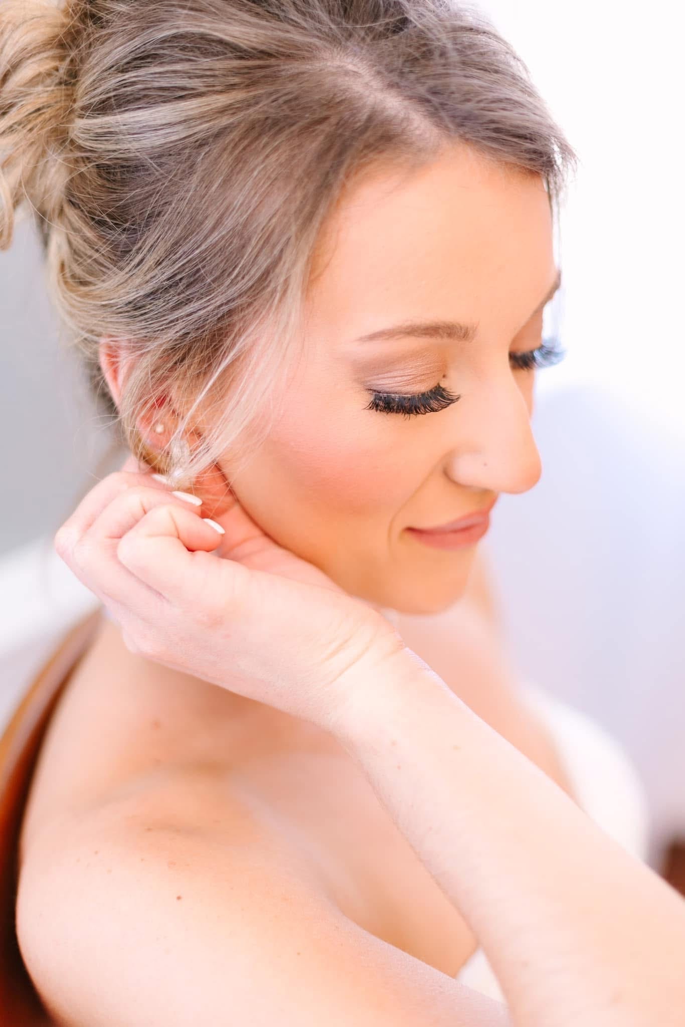 Bride in profile smiling softly while adjusting her earring during bridal preparations at Scarborough House wedding venue.