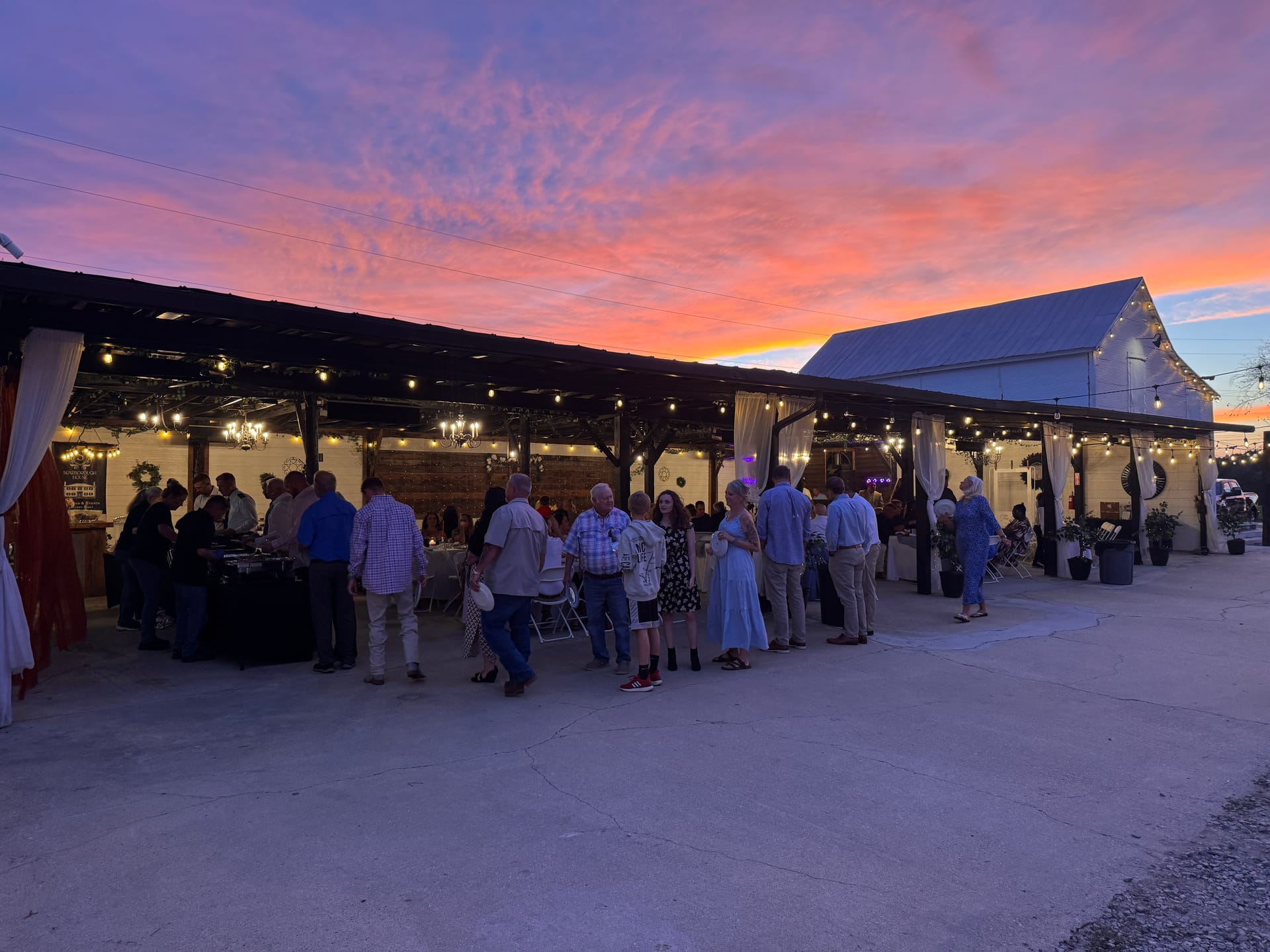 Guests mingle under a string-lit open-air pavilion at Scarborough House during a breathtaking pink and orange sunset reception.