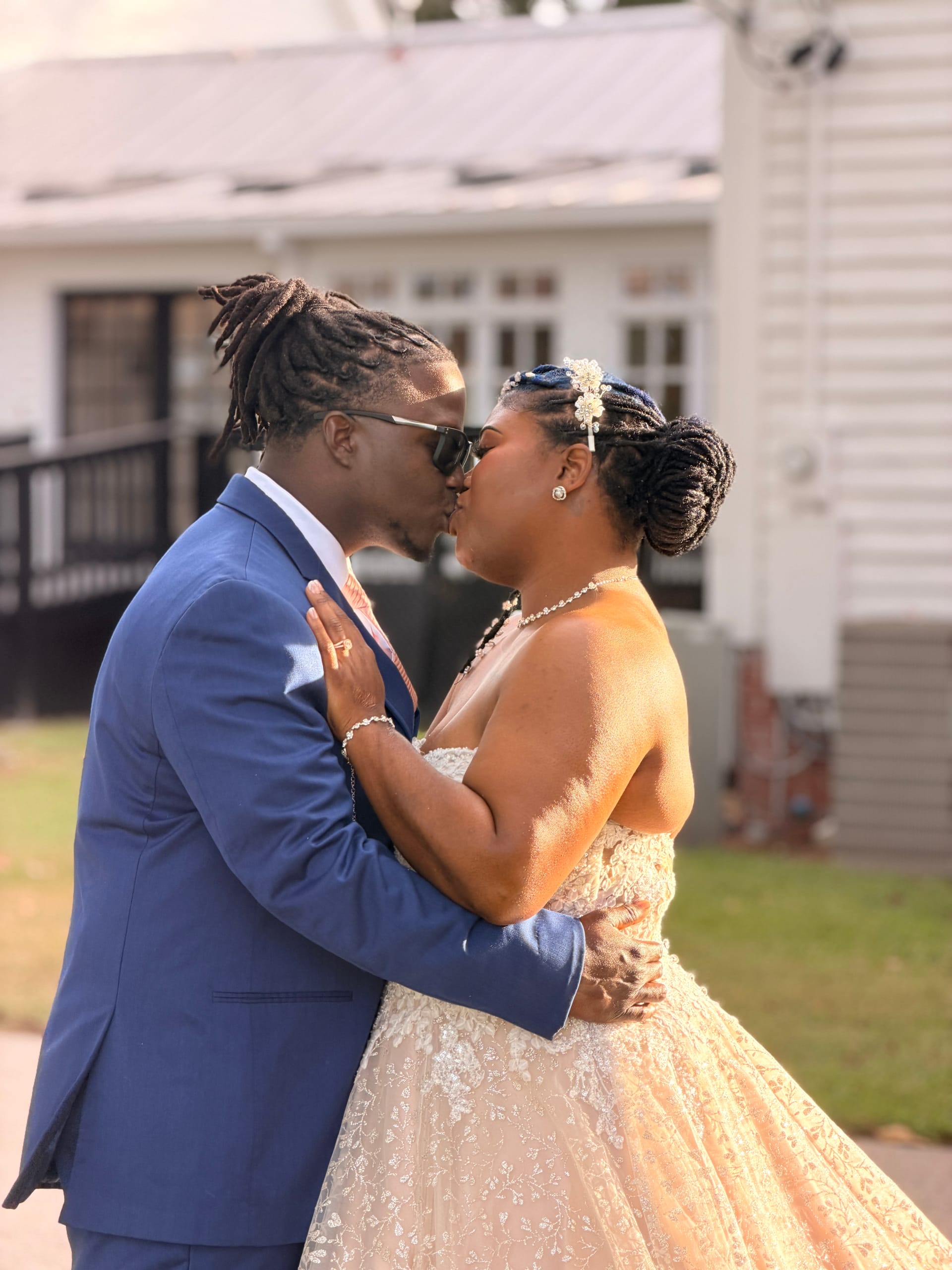 Bride in a champagne lace ball gown and groom in a blue suit share a kiss in front of the historic 1821 Scarborough House manor on their wedding day.