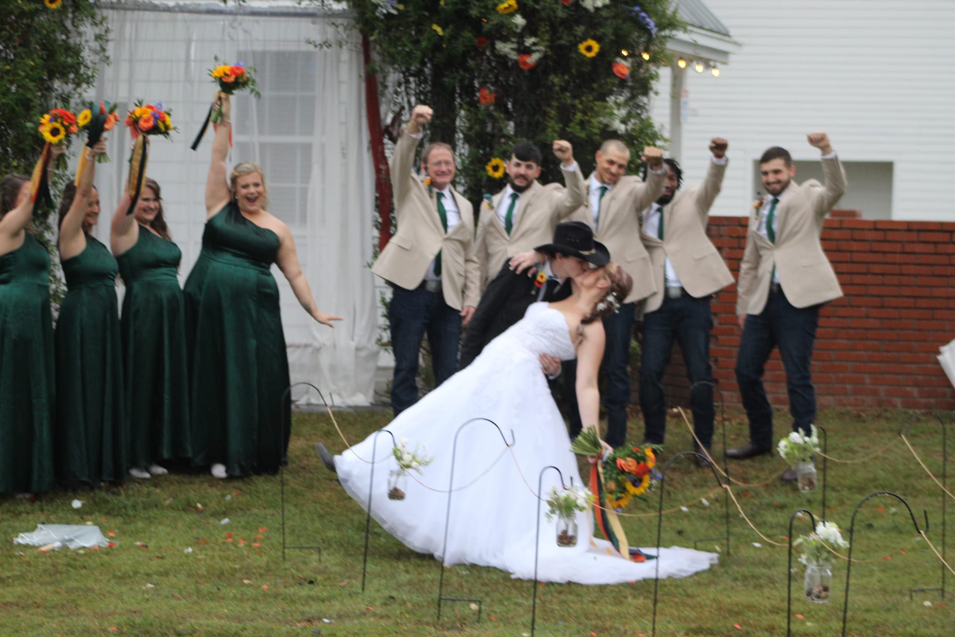 Groom dips bride for a kiss on the ceremony lawn while their cheering wedding party celebrates behind them at Scarborough House historic estate venue.