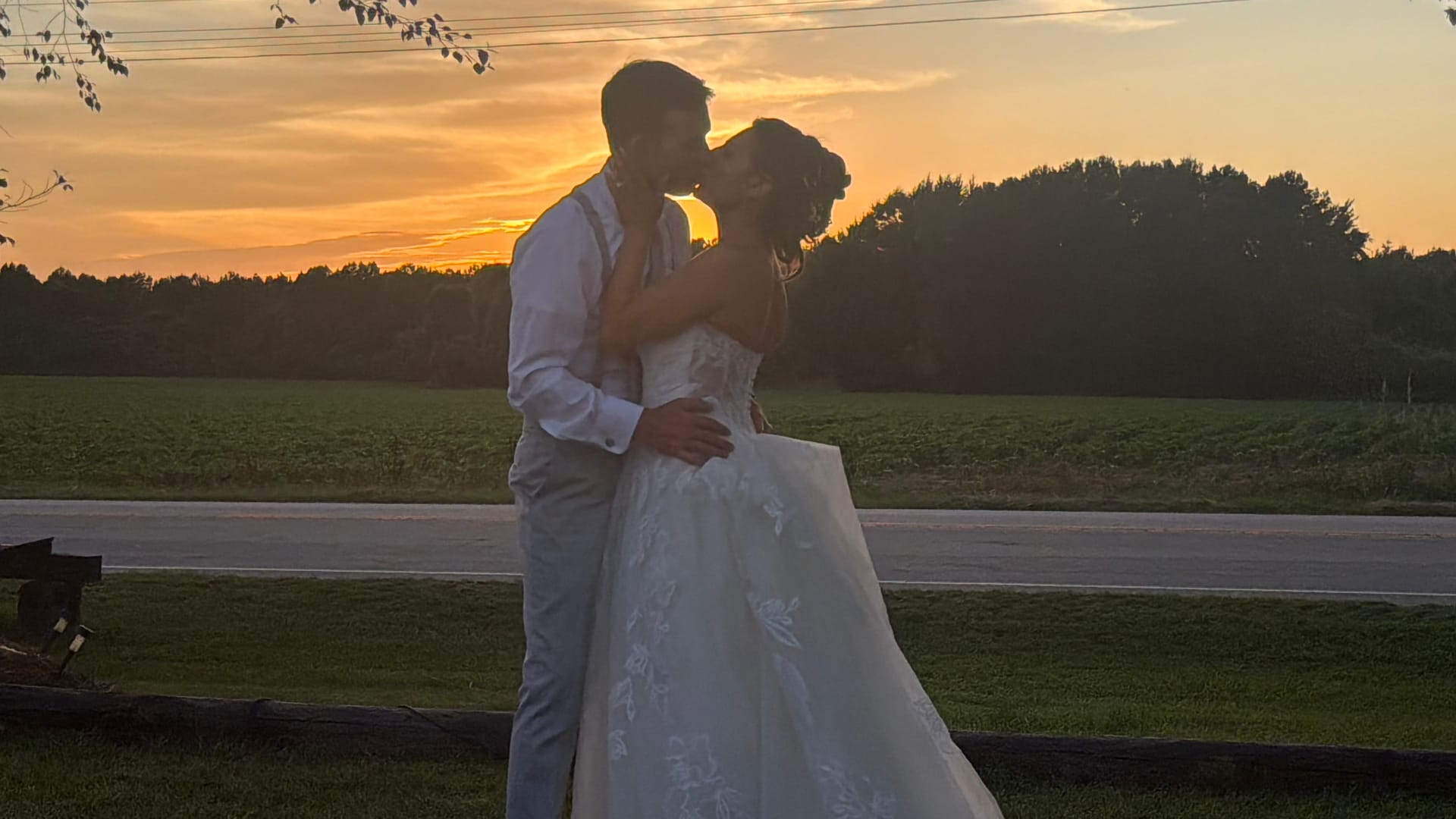 Bride and groom share a romantic kiss silhouetted against a glowing golden sunset over open farmland fields at Scarborough House estate.