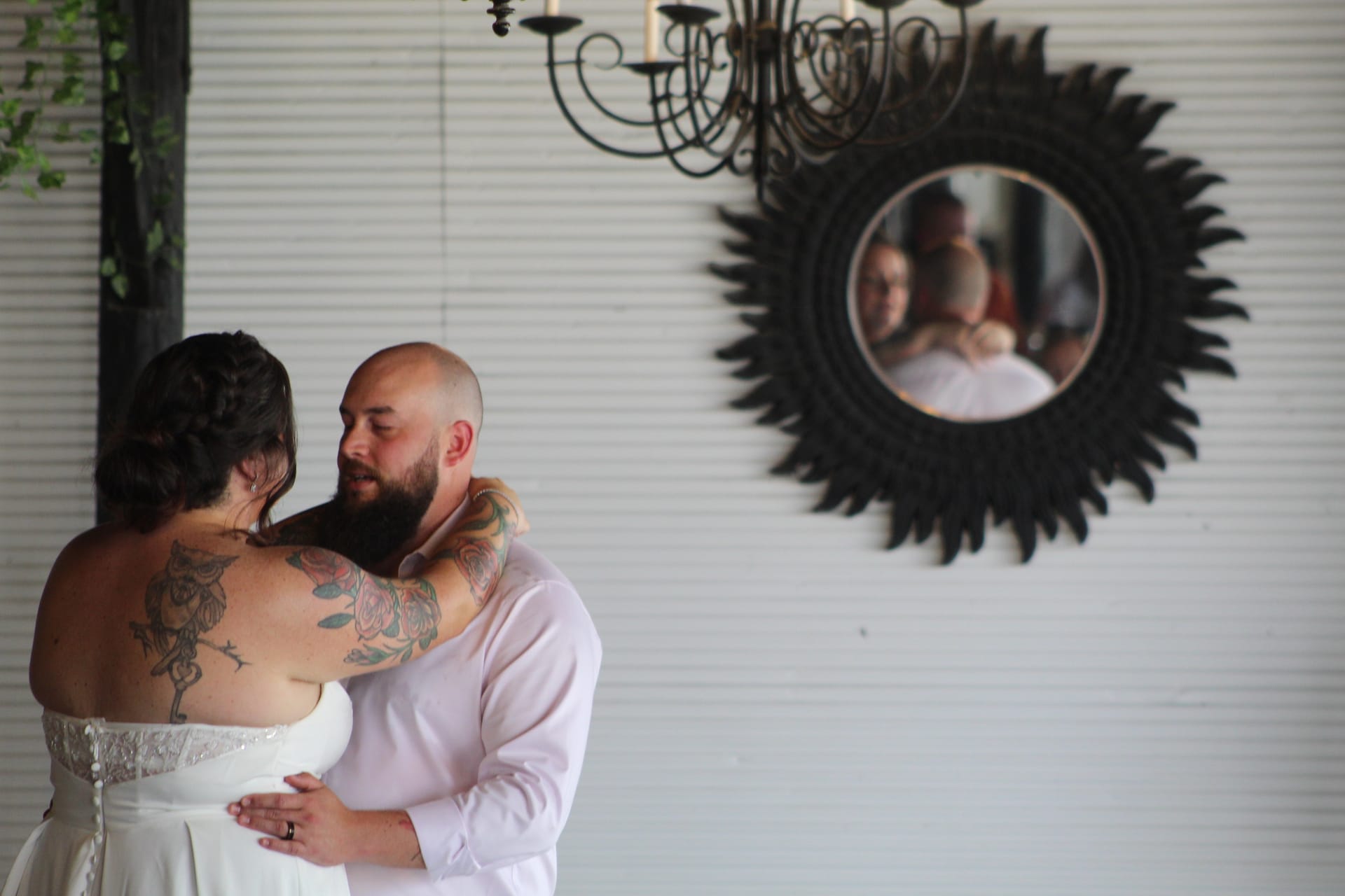 Bride and groom share an intimate embrace inside Scarborough House as their reflection appears in an ornate sunburst mirror beneath a wrought-iron chandelier.