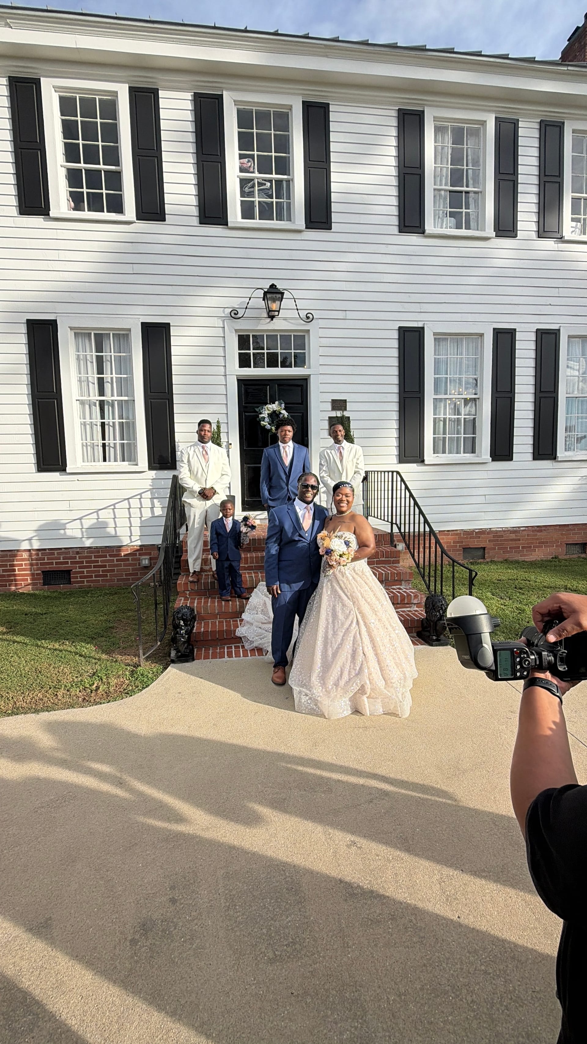 Bride in a white ballgown and groom in a navy suit pose with groomsmen and a ring bearer on the front steps of the 1821 Scarborough House historic manor.