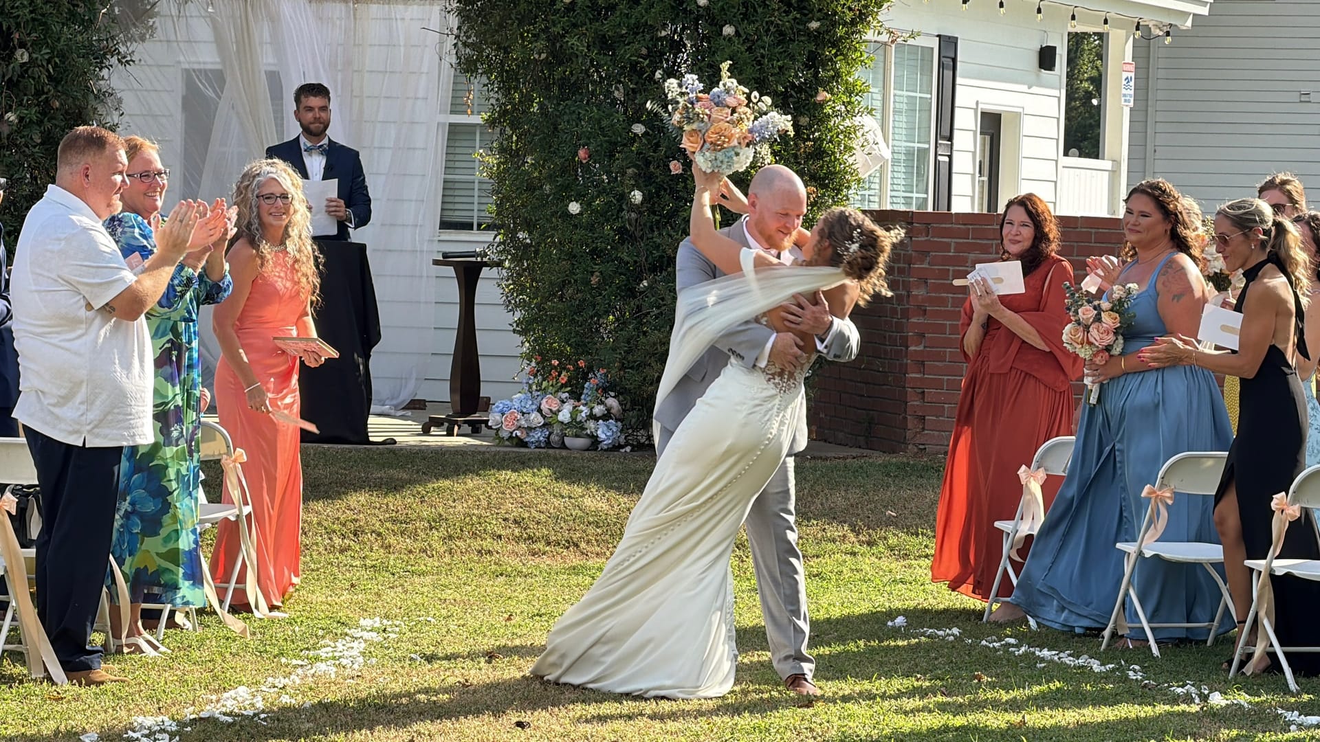 Groom dips his bride for a celebratory kiss as guests cheer along the aisle during an outdoor wedding ceremony at Scarborough House.