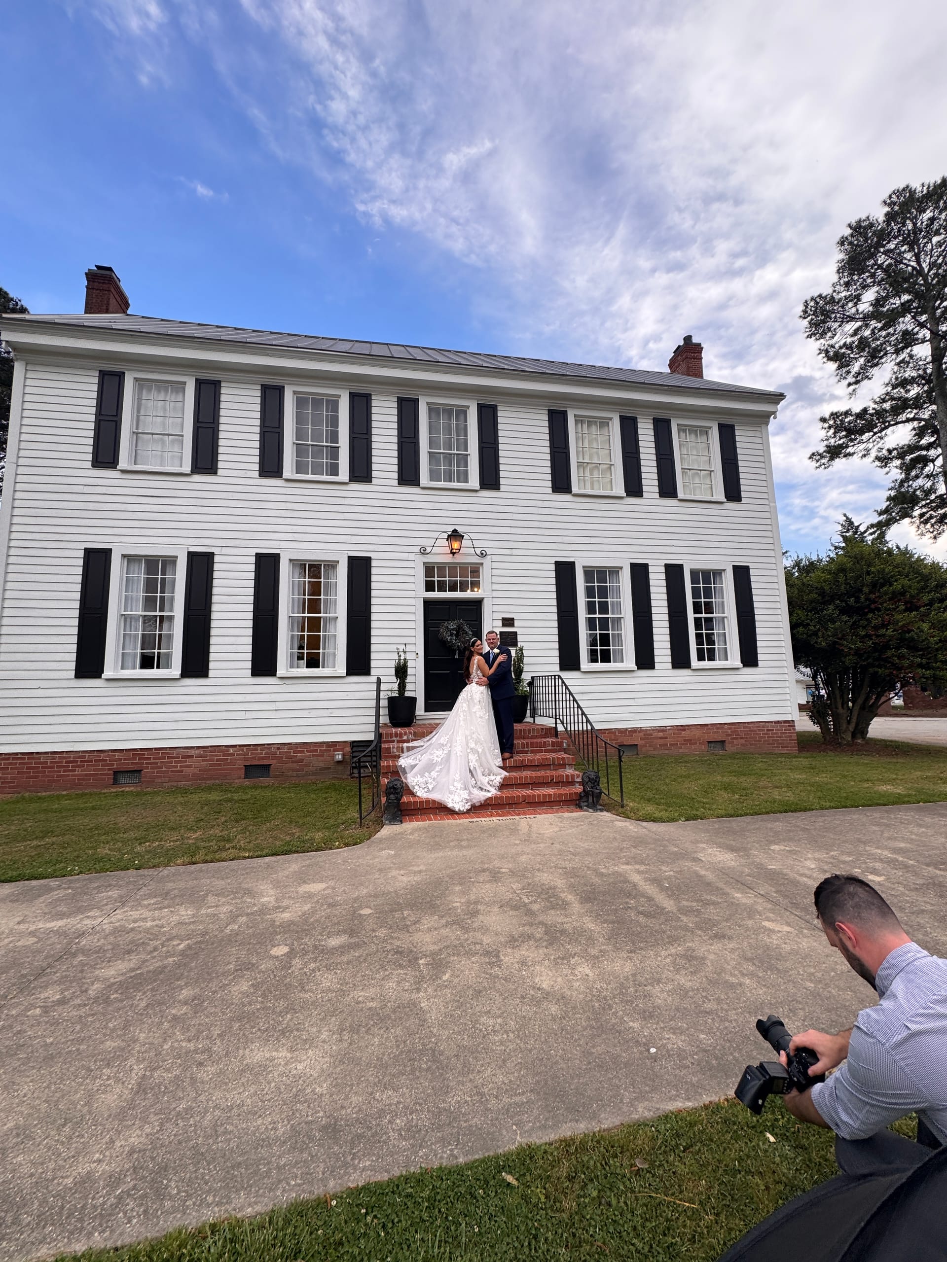 Bride and groom pose romantically on the brick front steps of the 1821 Scarborough House manor while a photographer captures the moment from the foreground.