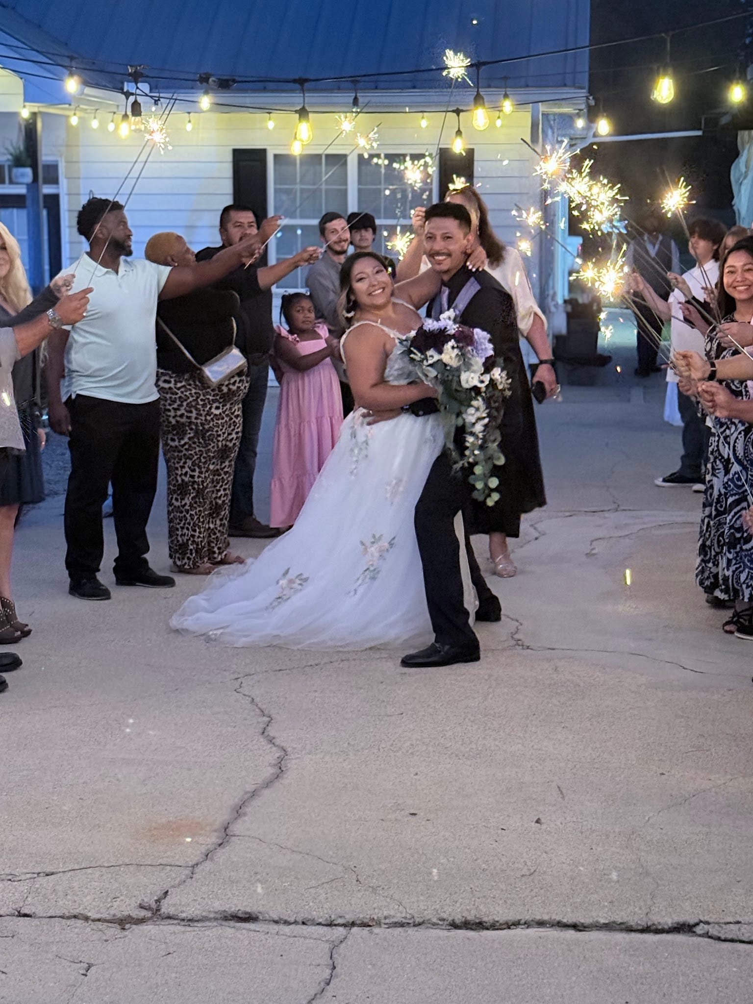 Bride and groom share a joyful dip pose during their sparkler send-off exit surrounded by cheering guests under warm string lights at a historic outdoor wedding venue.