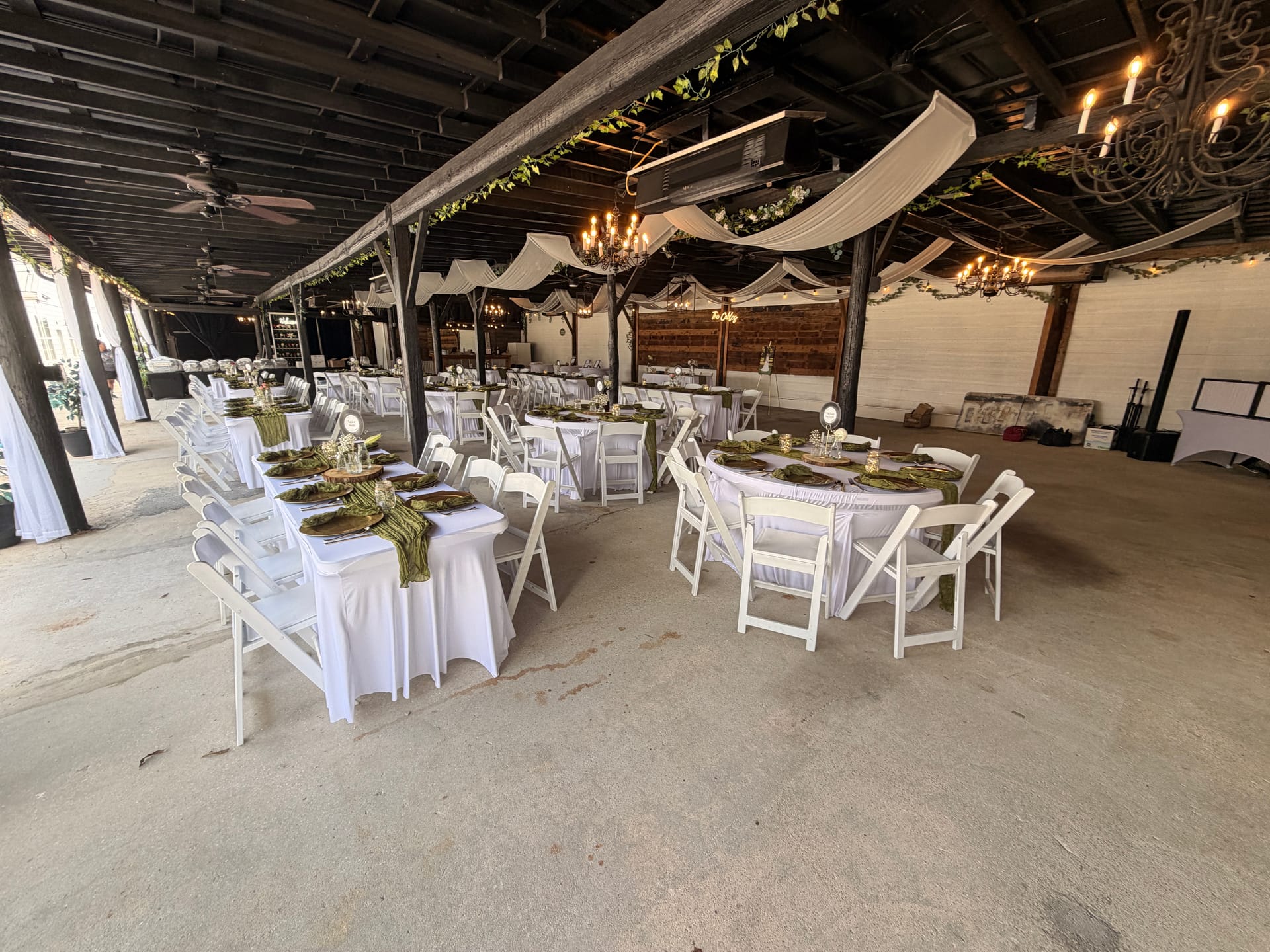 Elegantly decorated grand hall reception space at Scarborough House featuring round tables with white linens and green satin runners, white folding chairs, hanging chandeliers, and draped fabric ceiling accents.