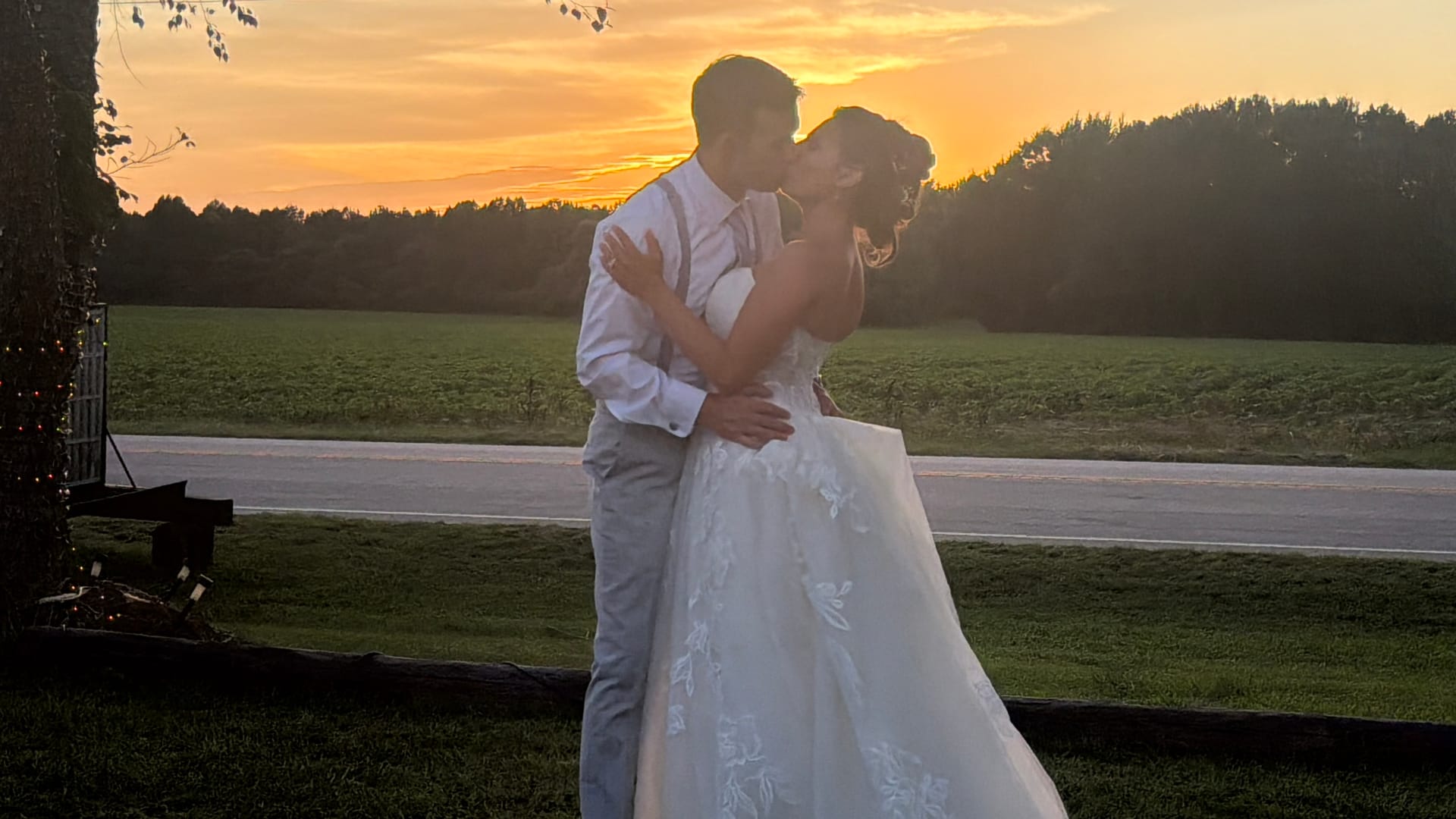 Bride and groom share a romantic kiss at sunset with a glowing orange sky and rolling farmland fields behind them at Scarborough House wedding venue.