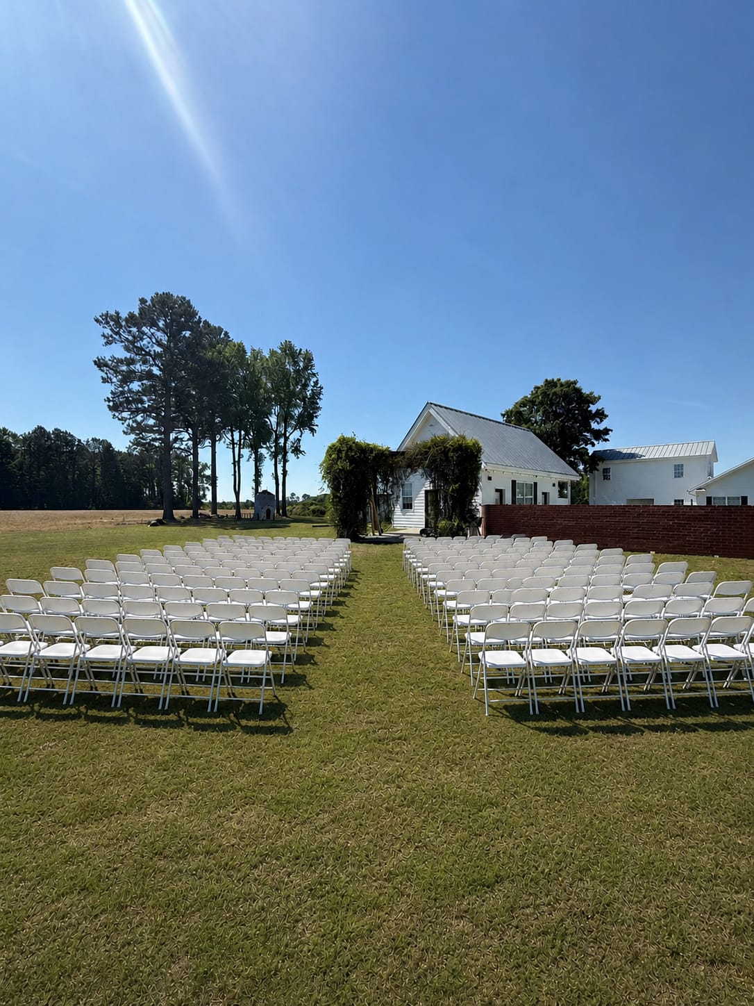 Rows of white folding chairs arranged in two sections on a sunny green lawn leading to a vine-covered white manor house at Scarborough House wedding venue.