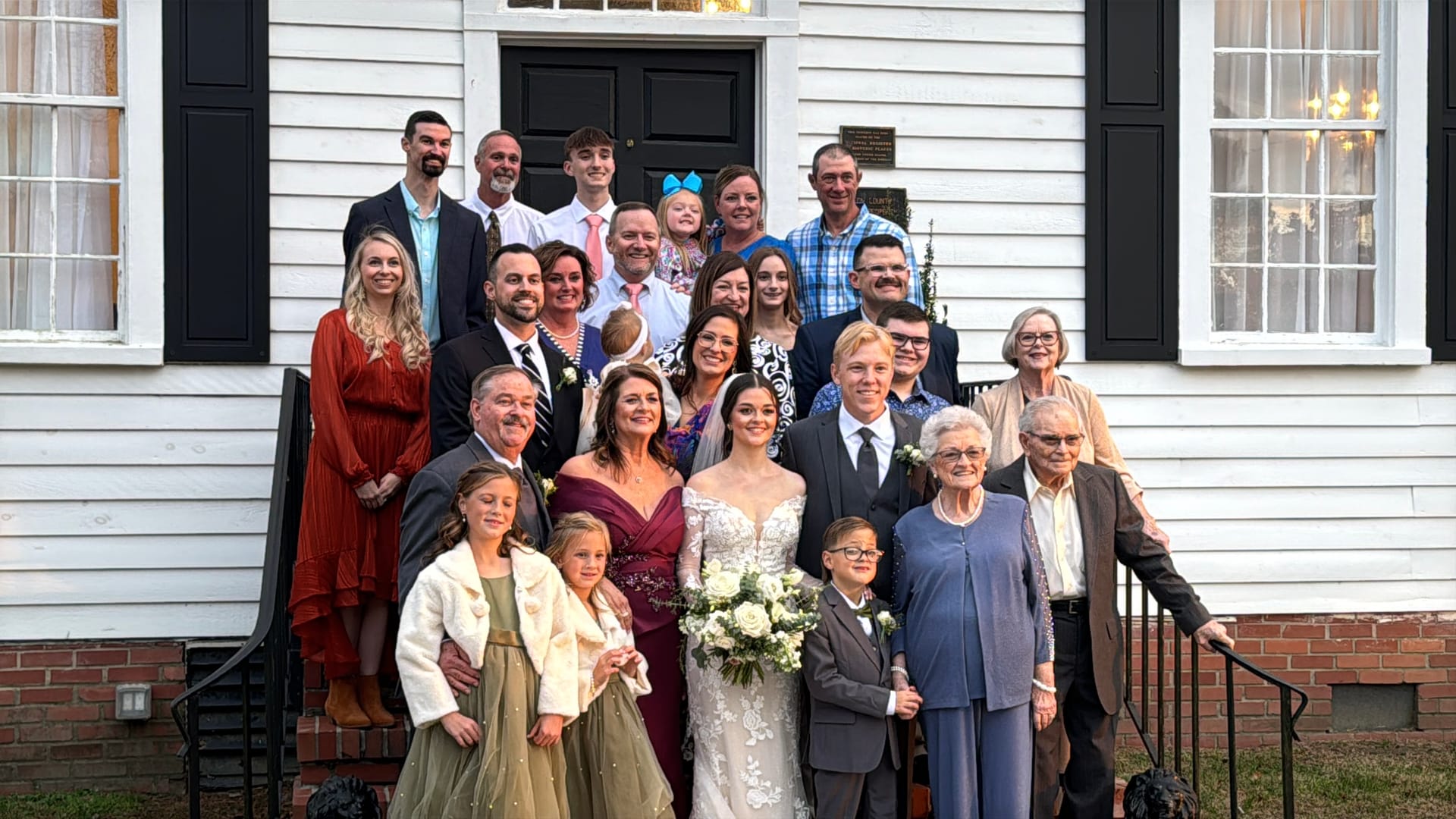 Bride and groom surrounded by a large multi-generational family group posed on the white clapboard front steps of the historic 1821 Scarborough House manor.