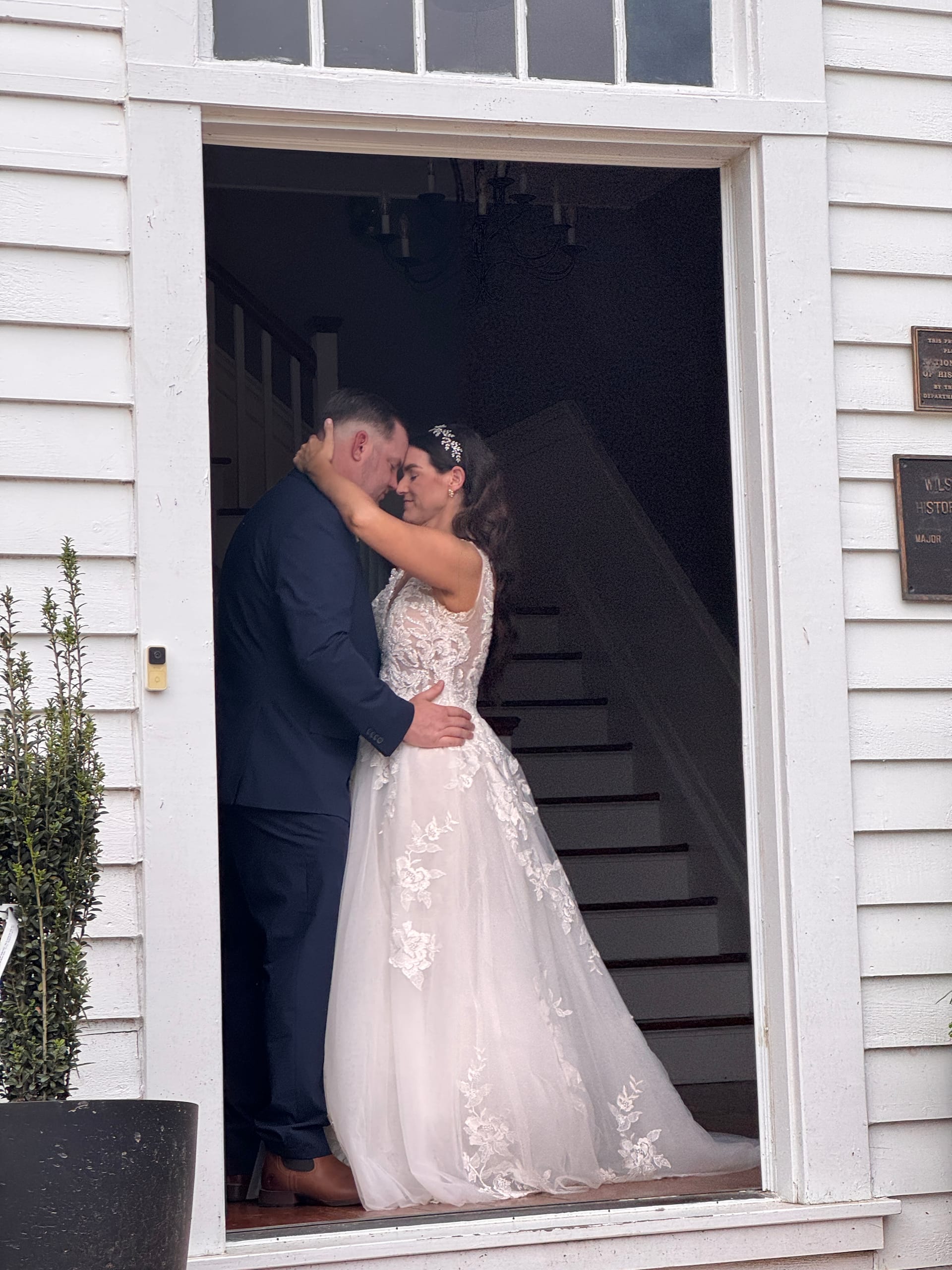 Bride and groom sharing an intimate forehead-touch embrace in the white-framed doorway of the historic 1821 Scarborough House manor.
