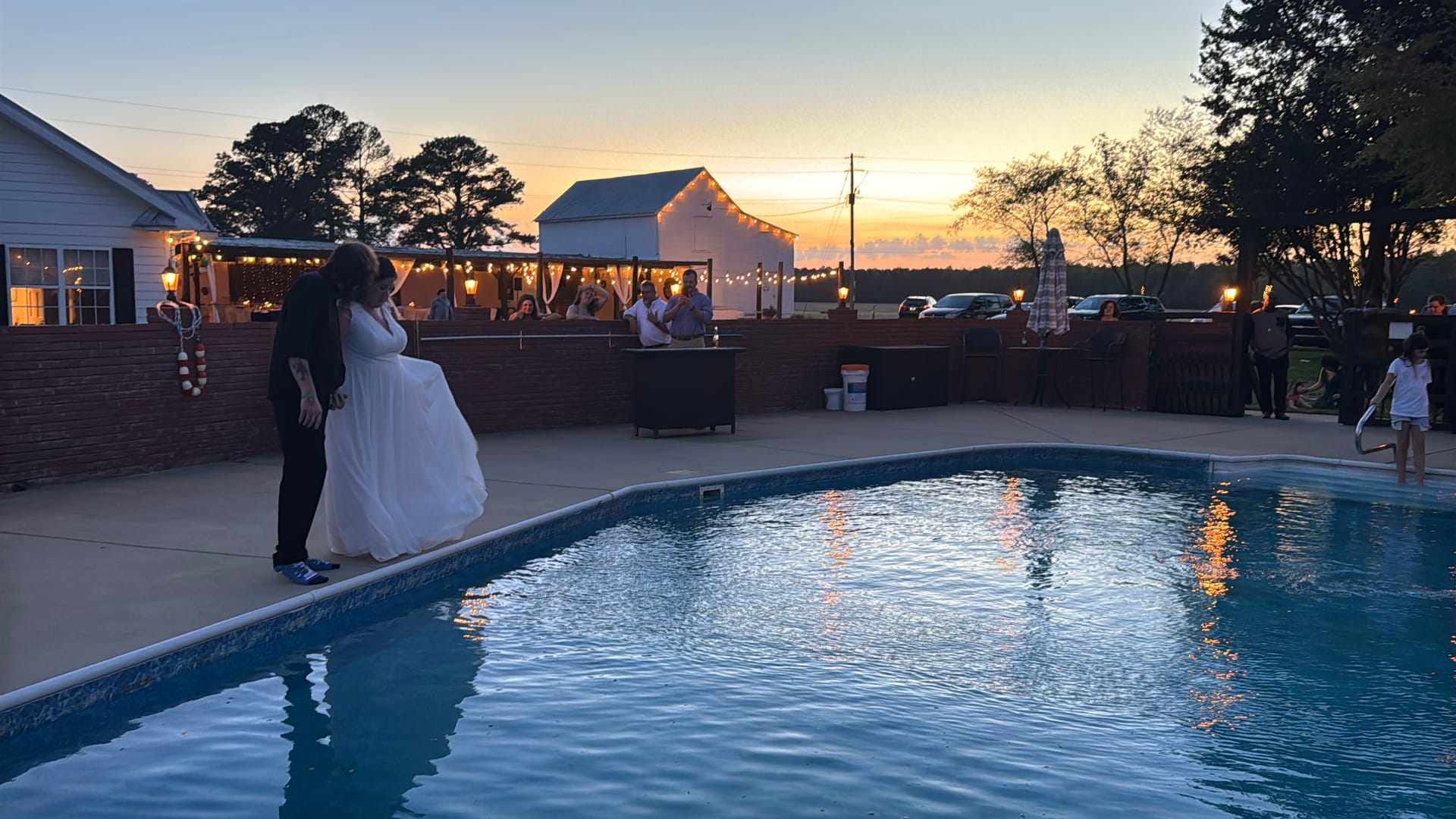Bride and groom share a romantic dance beside the pool at sunset with string lights and a white barn glowing in the background at Scarborough House.