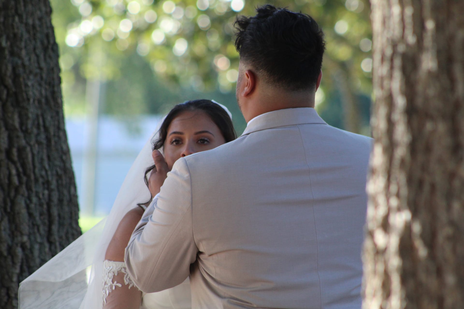 Bride with tearful eyes looks up at groom during an emotional first-look moment among the oak trees at Scarborough House wedding venue.