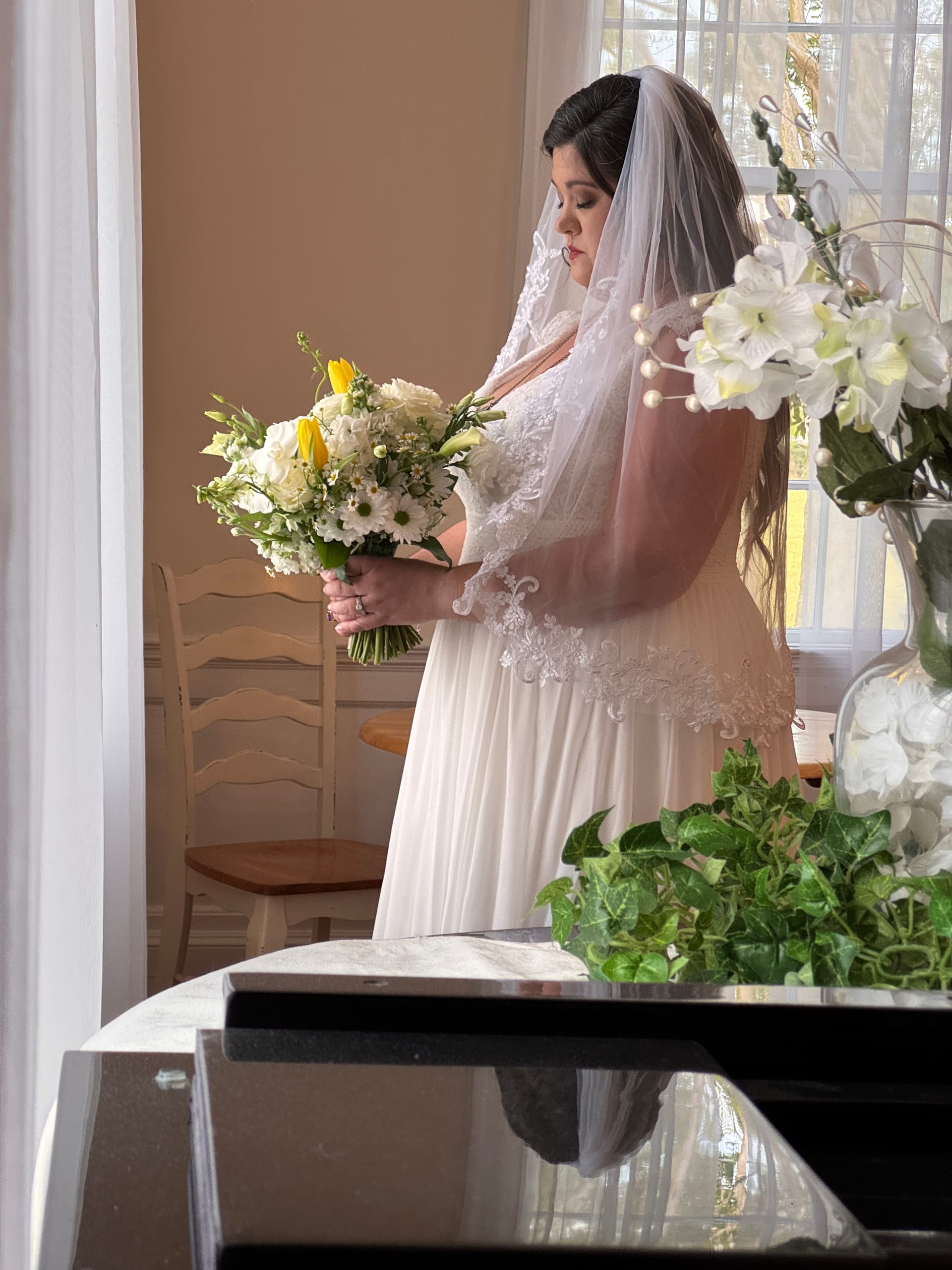 Bride in a white lace-trimmed gown and cathedral veil gazes down at her white and yellow bridal bouquet in a softly lit room at Scarborough House.