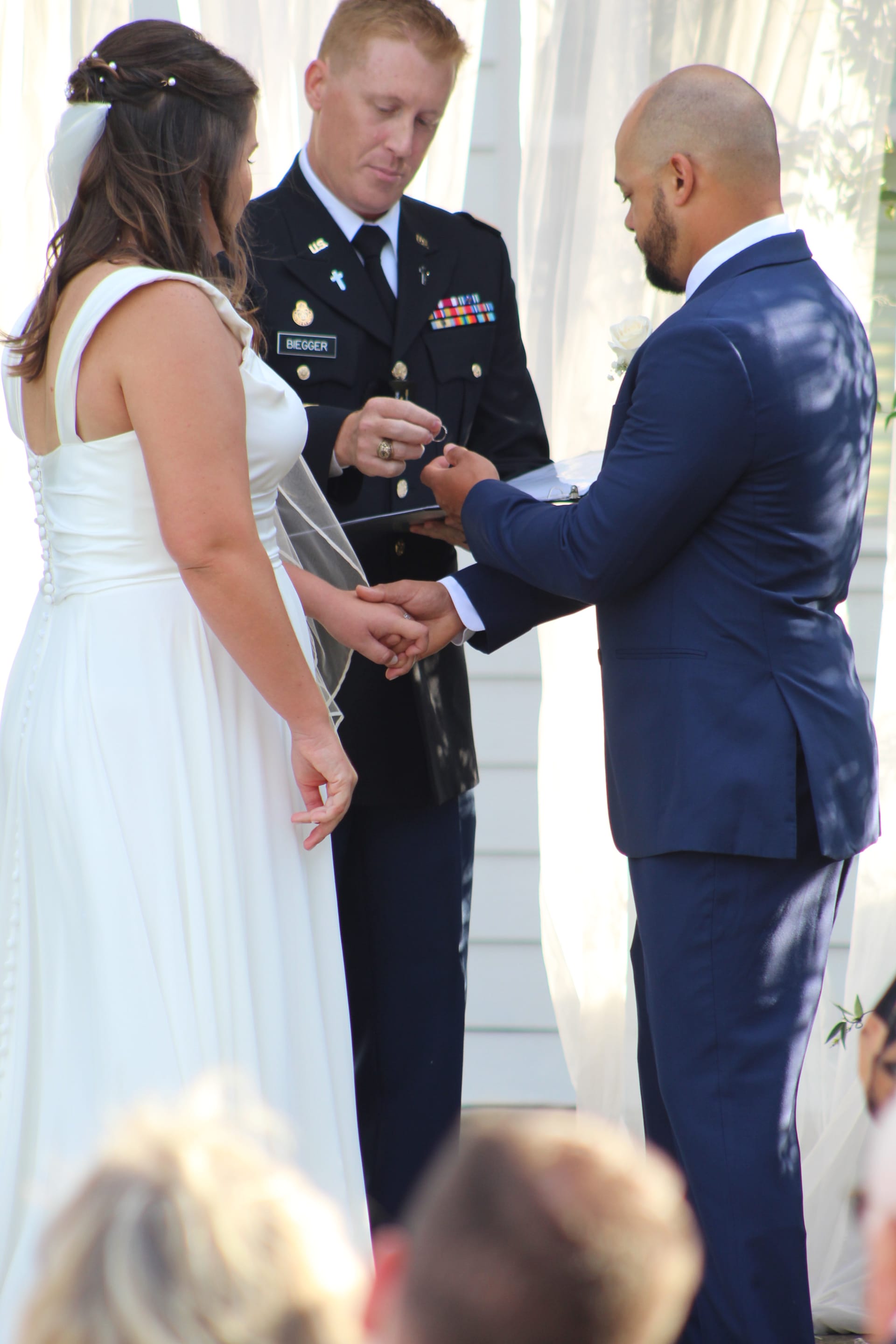 Bride in white gown and groom in navy suit exchange rings during an outdoor wedding ceremony officiated by a decorated military officer at Scarborough House.