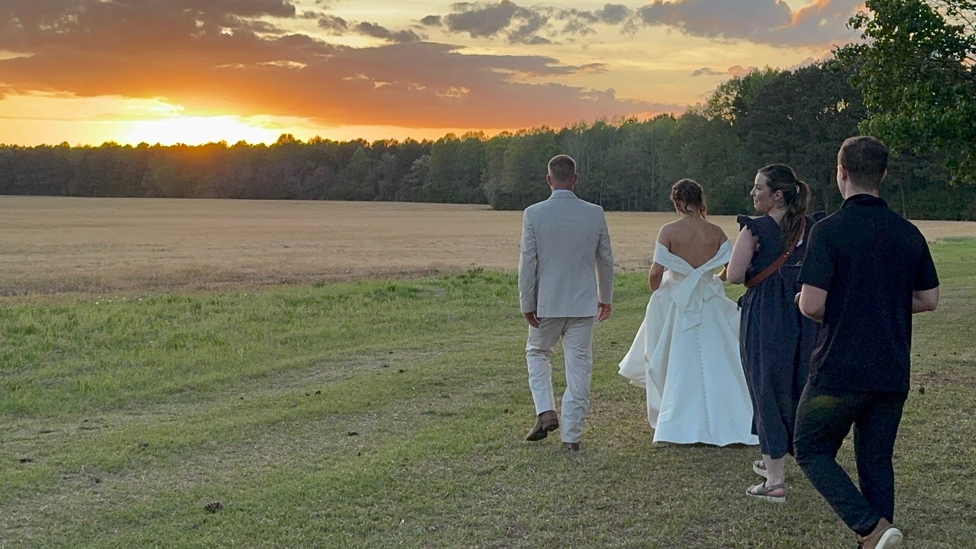 Bride and groom walk toward a glowing golden sunset over open farmland fields at Scarborough House accompanied by their wedding photographers.