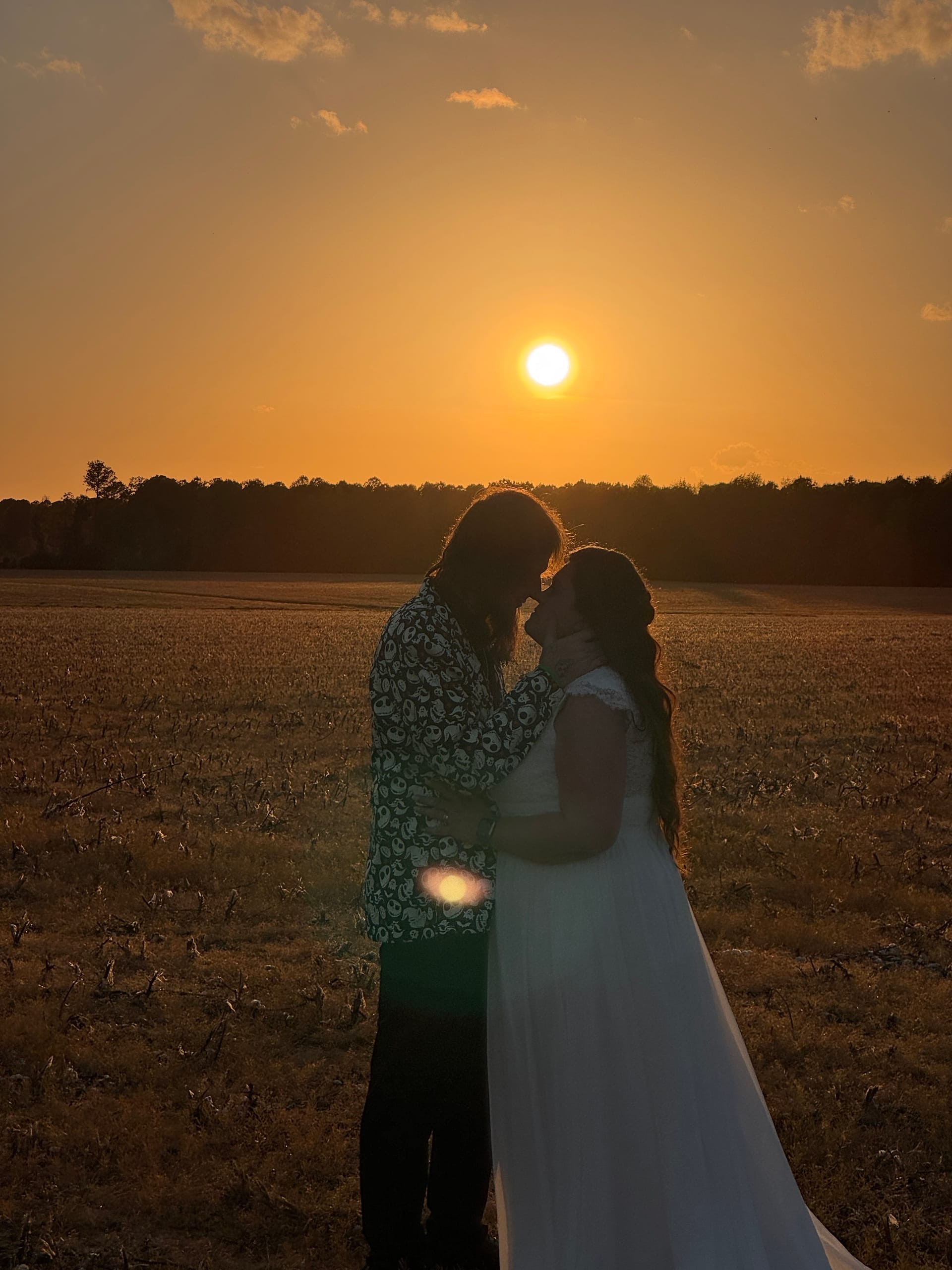 Bride and groom share an intimate moment silhouetted against a glowing golden sunset over open farmland fields at Scarborough House.