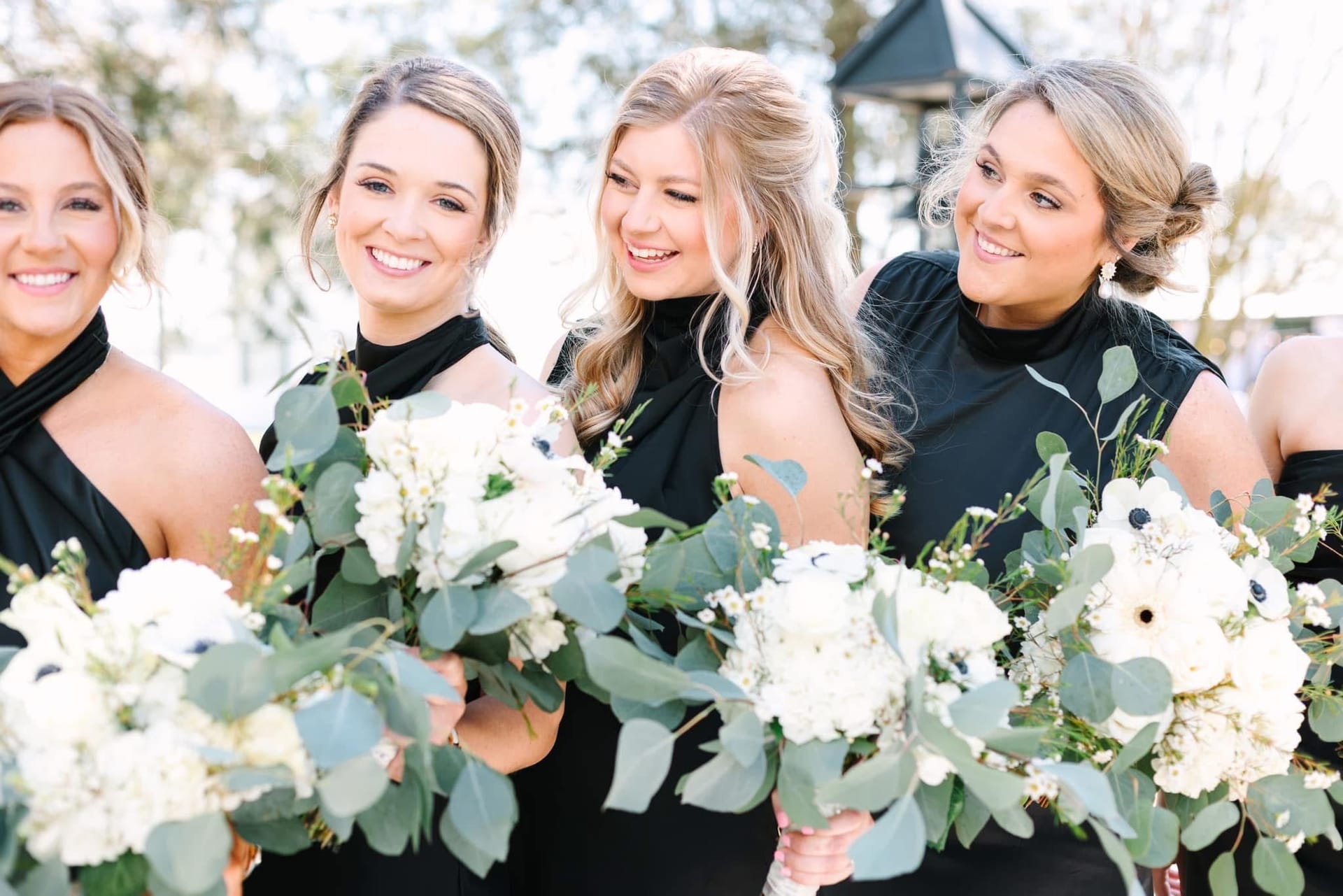 Four bridesmaids in black halter gowns laughing together while holding white floral and eucalyptus bouquets at Scarborough House wedding venue.