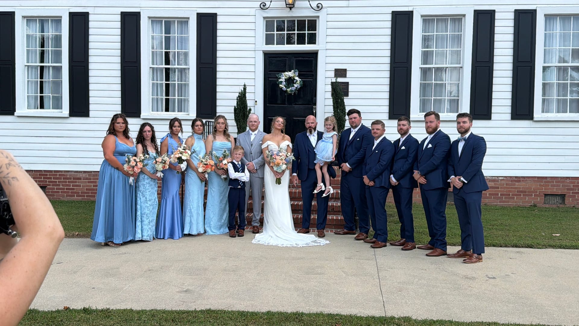 Full wedding party posed on the front steps of the 1821 Scarborough House manor, bridesmaids in powder blue gowns and groomsmen in navy suits flanking the bride and groom.
