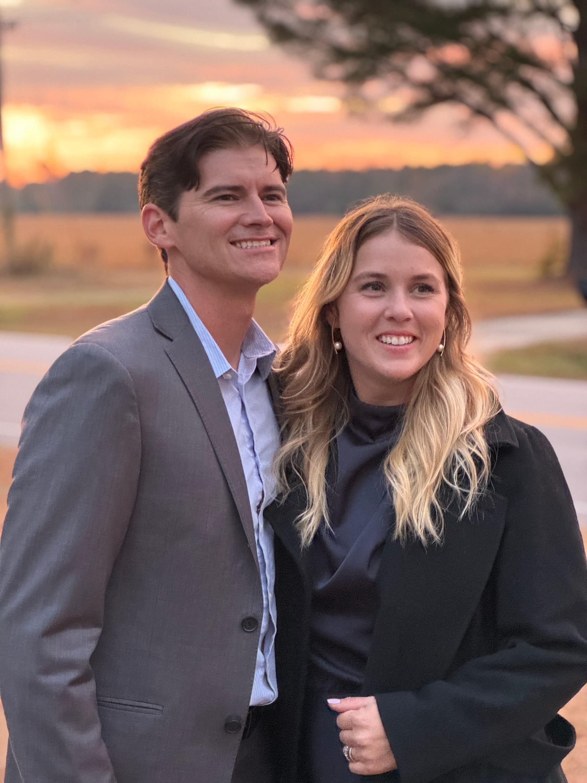 Smiling couple posed together at sunset with warm orange skies and open farmland fields in the background at Scarborough House.