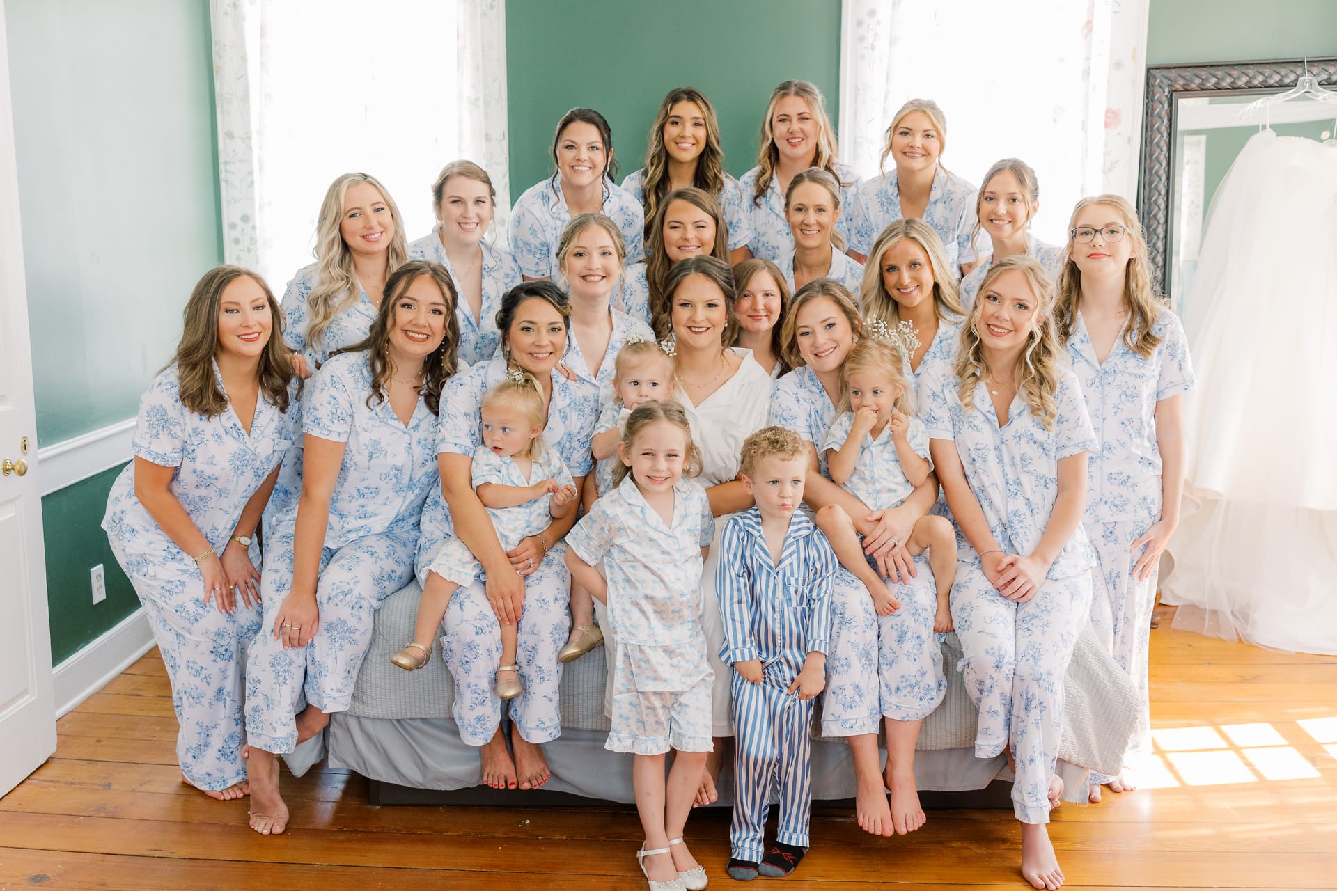 Bride surrounded by bridesmaids and young children all wearing matching blue floral pajamas in a bright green-walled bridal suite at Scarborough House.