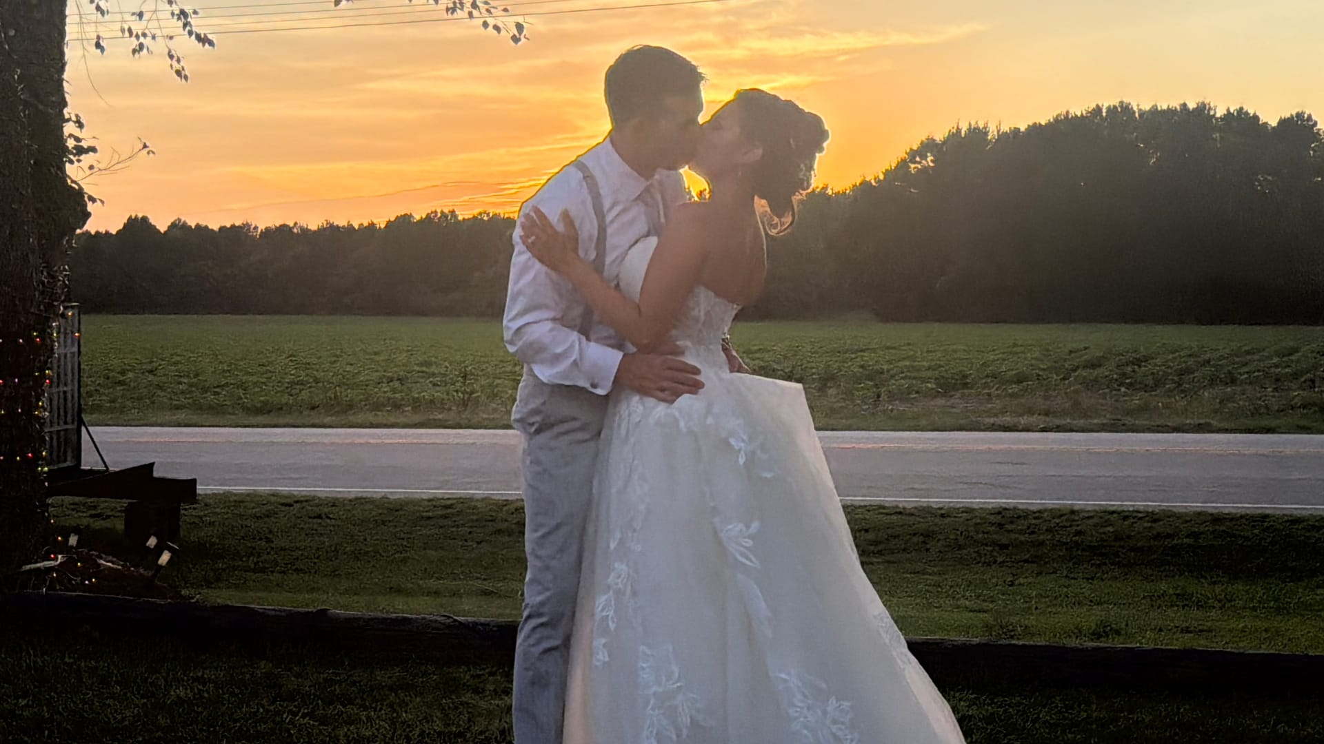 Bride and groom share a romantic kiss silhouetted against a glowing golden sunset over open farmland fields at Scarborough House estate.