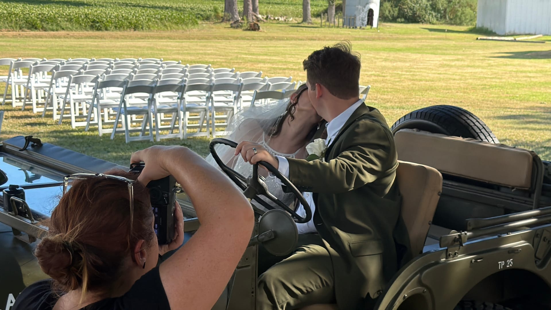 Bride and groom share a kiss while seated in a vintage military jeep on the ceremony lawn at Scarborough House, with rows of white folding chairs and lush green fields visible in the background.