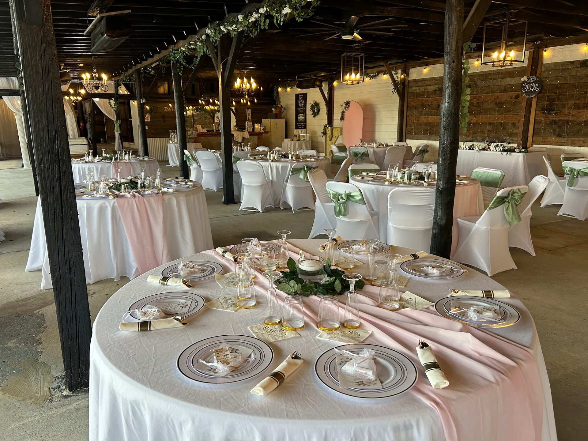 Elegantly set round reception tables with blush pink runners, white linens, layered charger plates, and greenery centerpieces inside the rustic grand hall at Scarborough House.