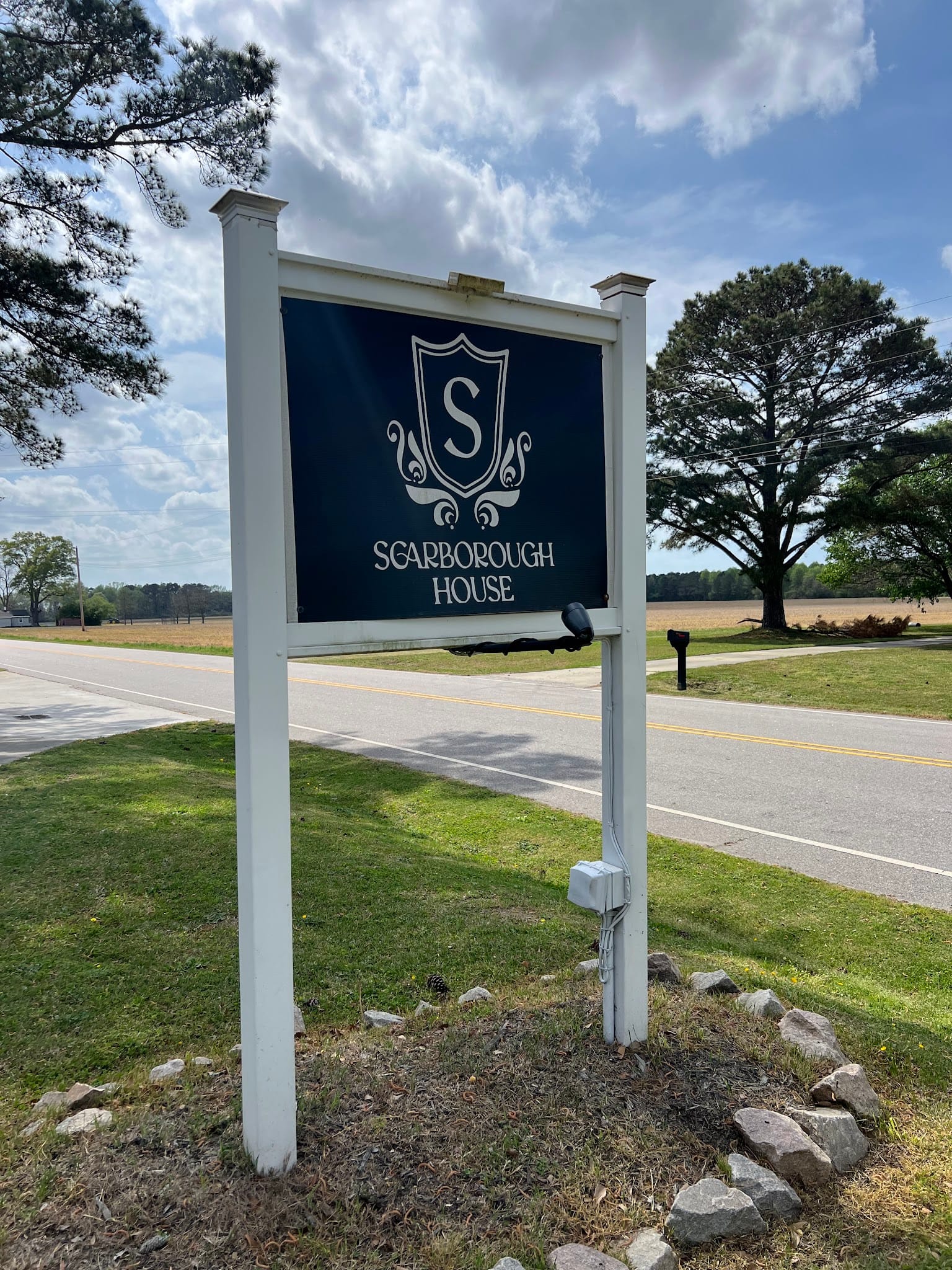 Scarborough House estate wedding venue sign with navy background and decorative crest logo displayed on white wooden posts along a rural road.