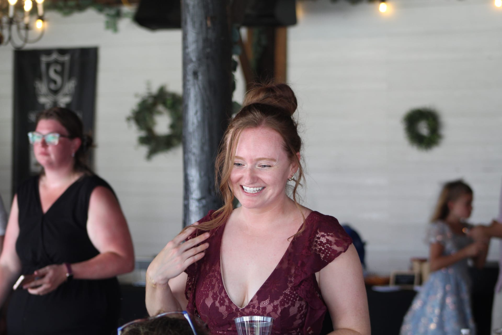 A smiling bridesmaid in a burgundy lace dress laughs candidly during the wedding reception inside the grand hall at Scarborough House, with greenery wreaths and warm string lights visible in the background.