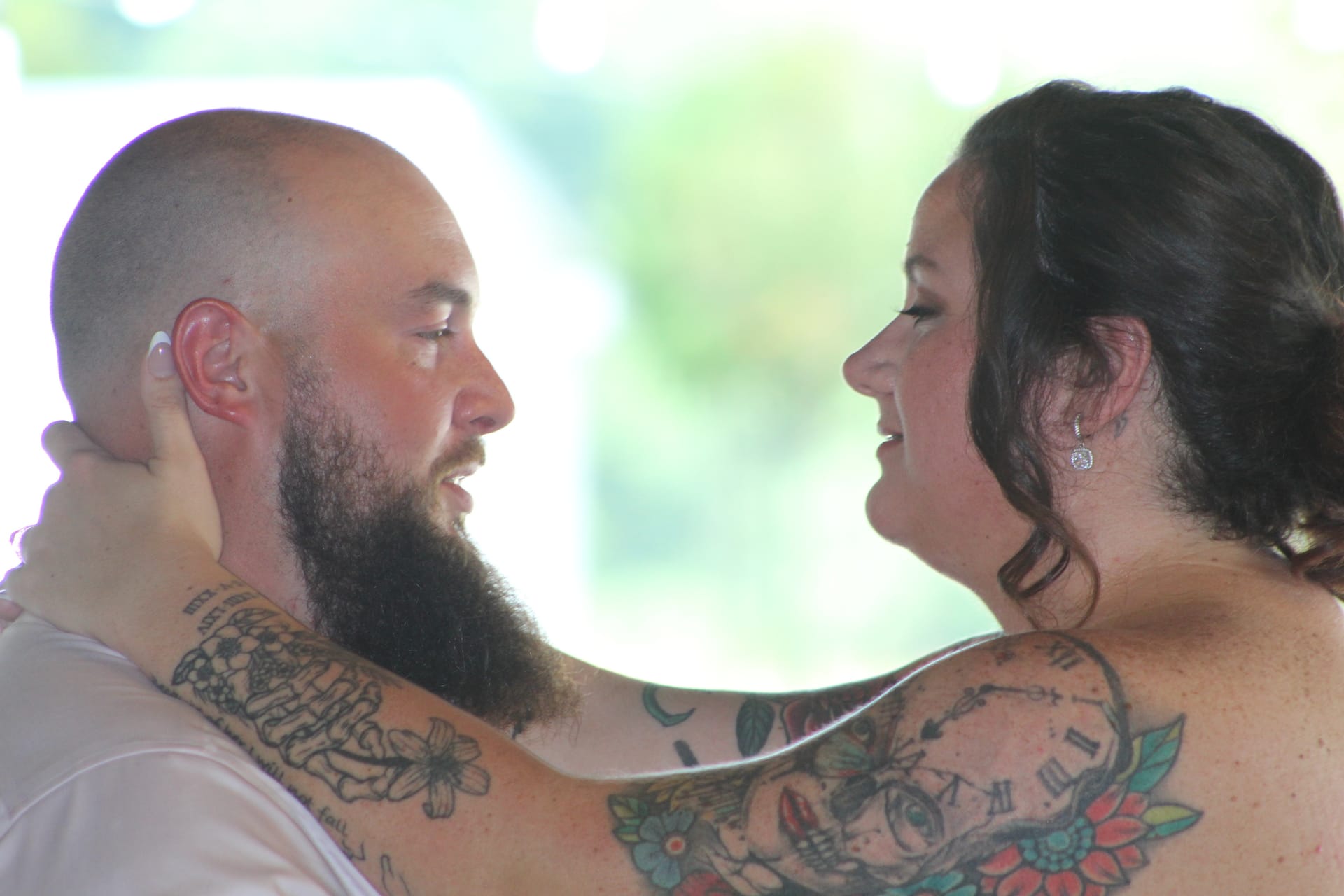 Tattooed bride and groom sharing an intimate face-to-face moment outdoors at Scarborough House wedding venue with soft green bokeh background.