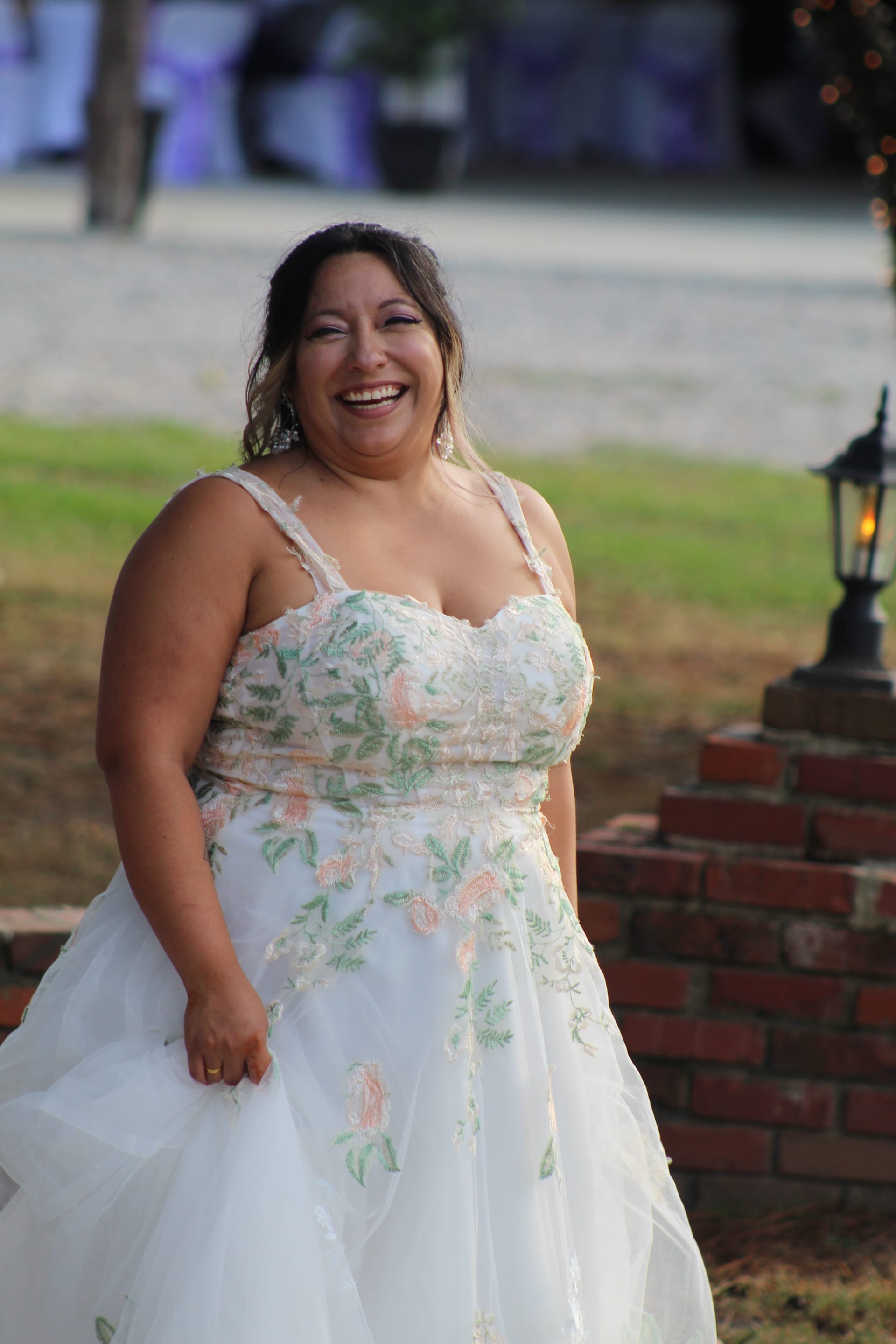 A joyfully laughing bride in a white floral embroidered gown stands on the ceremony lawn at Scarborough House historic estate venue.