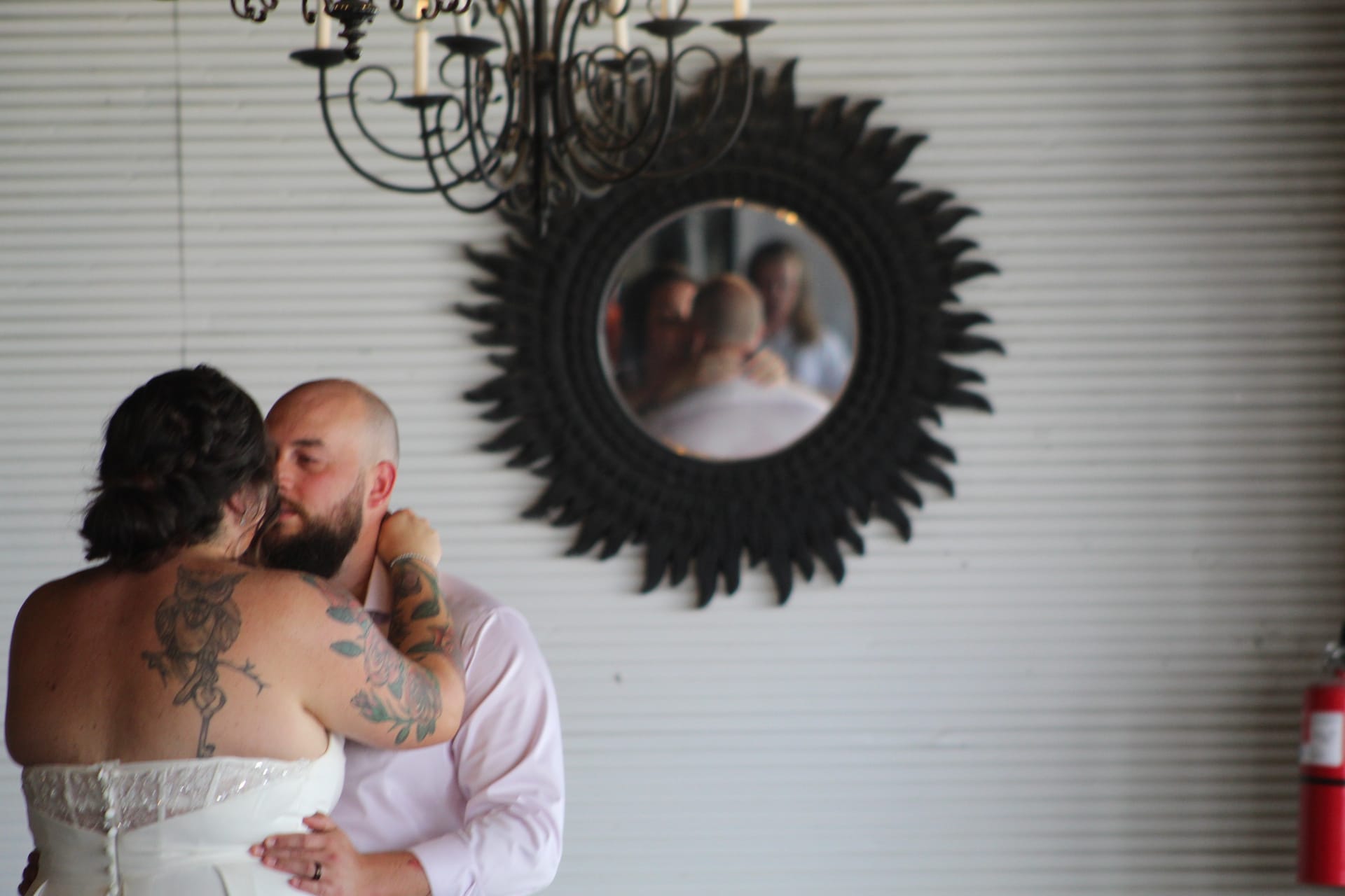 A bride and groom share an intimate embrace on the dance floor of Scarborough House grand hall, their reflections captured in an ornate sunburst mirror on the white shiplap wall beneath a wrought iron chandelier.