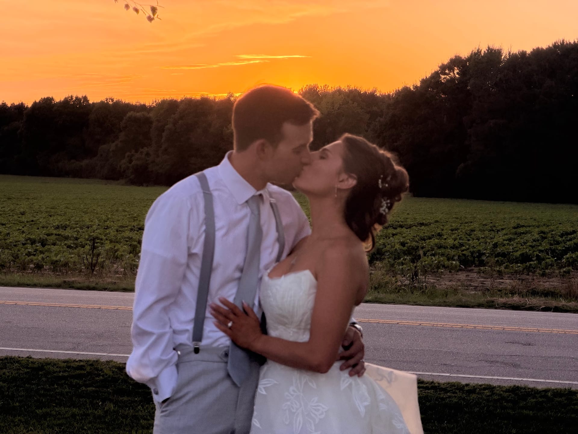 Bride and groom share a romantic kiss silhouetted against a vibrant orange sunset sky over the farmland fields at Scarborough House.