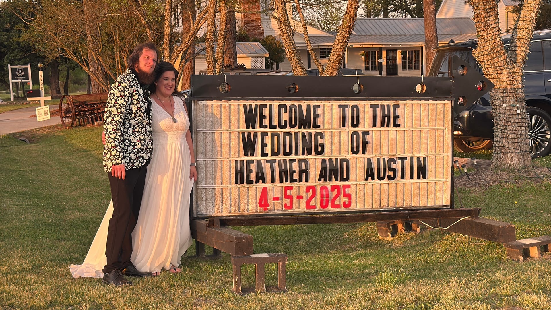 Bride in a white gown and groom in a patterned blazer pose beside an illuminated marquee sign welcoming guests to the wedding of Heather and Austin on April 5 2025 at the historic Scarborough House estate.