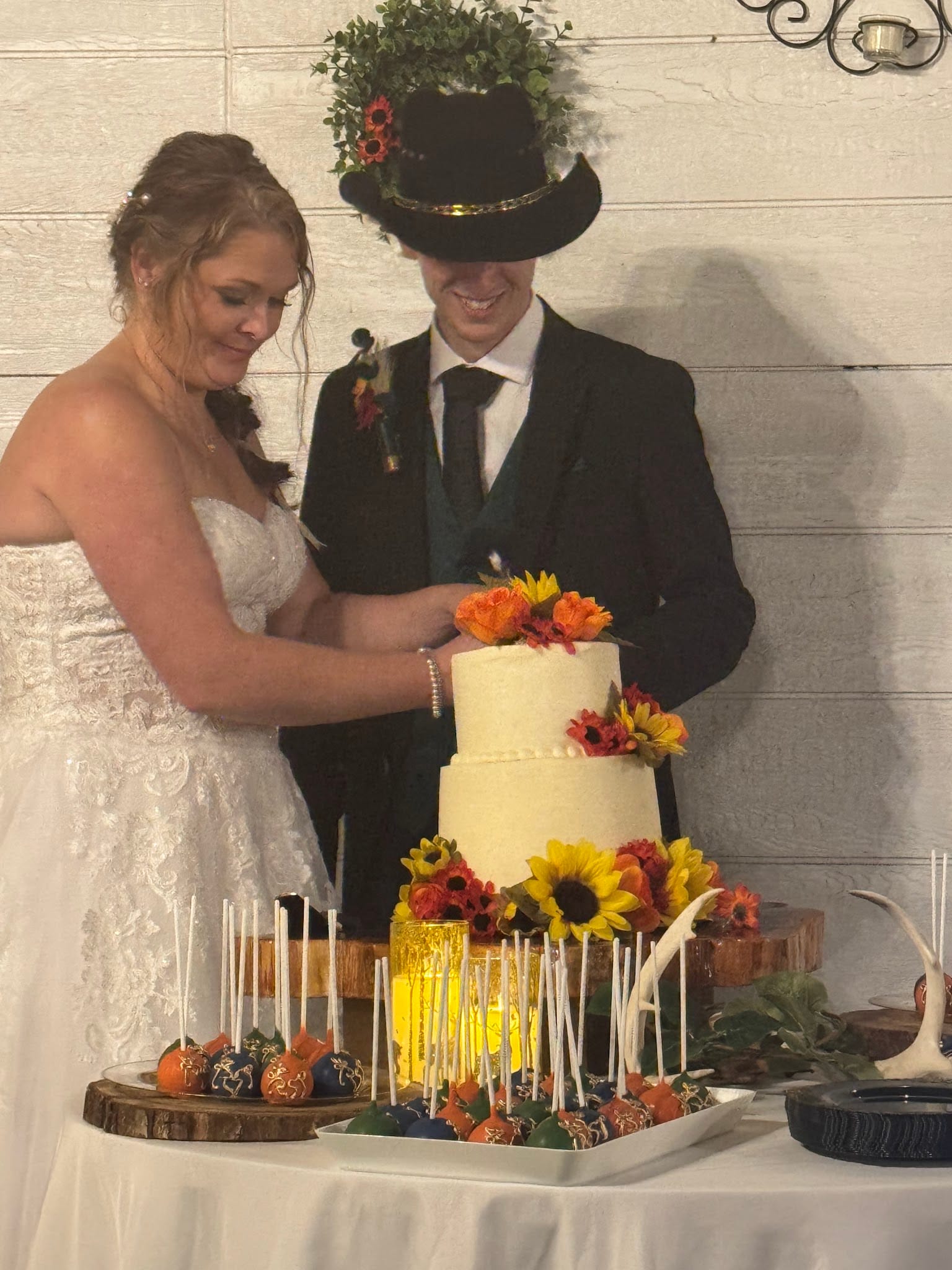 Bride and groom cutting their two-tier white wedding cake decorated with sunflowers and autumn blooms surrounded by colorful cake pops at Scarborough House.