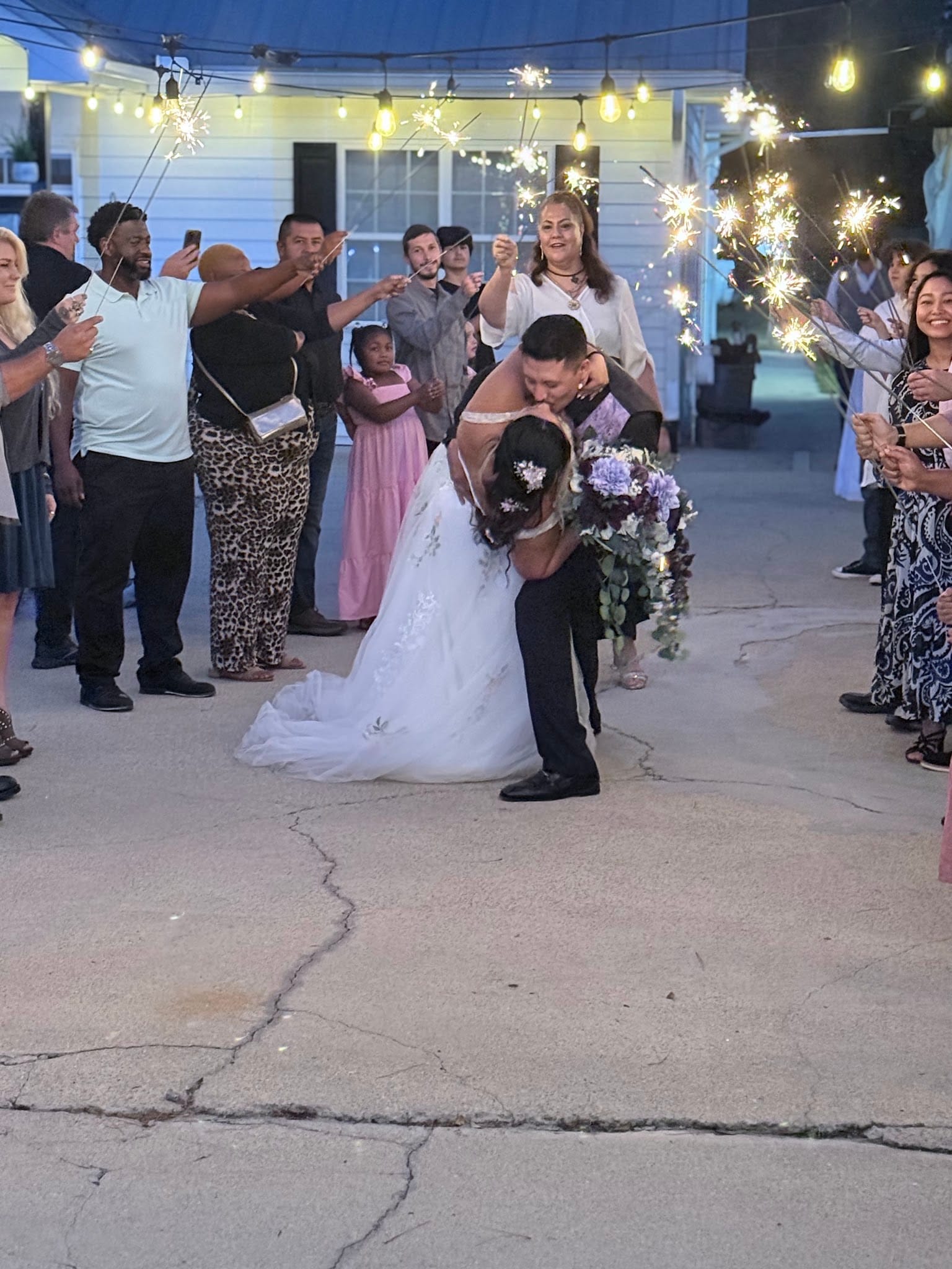 Bride and groom share a dramatic dip kiss during a sparkler exit surrounded by cheering guests under warm string lights at Scarborough House historic estate venue.