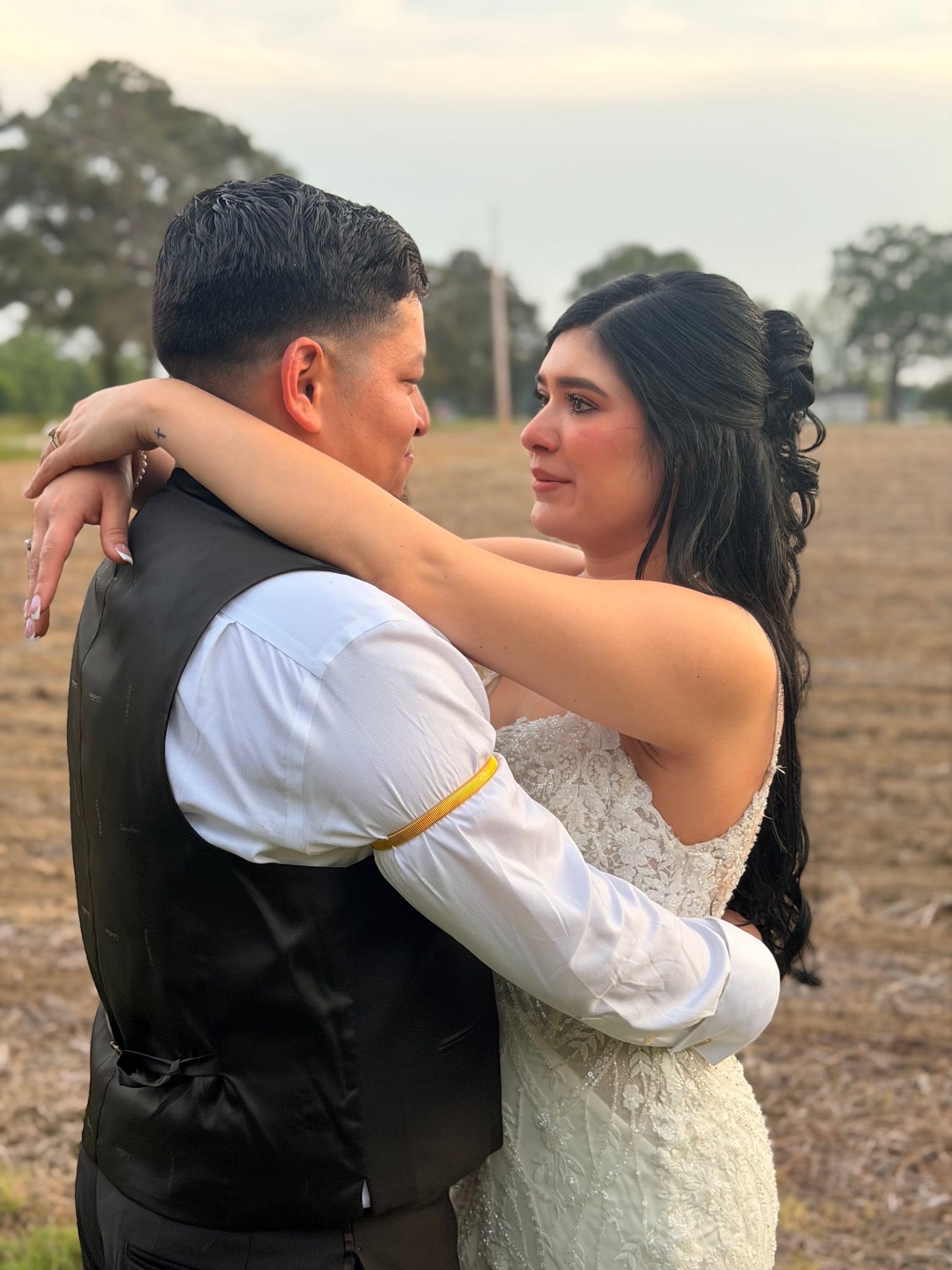 Tearful bride in lace gown embraces groom in black vest during an emotional outdoor portrait in the open farmland fields at Scarborough House.