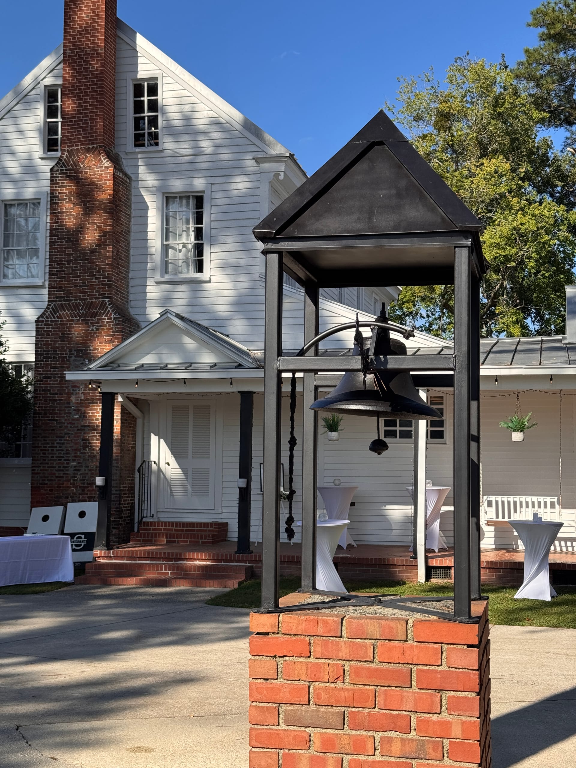 Historic black iron bell tower on a brick pedestal in front of the 1821 Scarborough House manor with white cocktail tables and event decor visible on the porch.