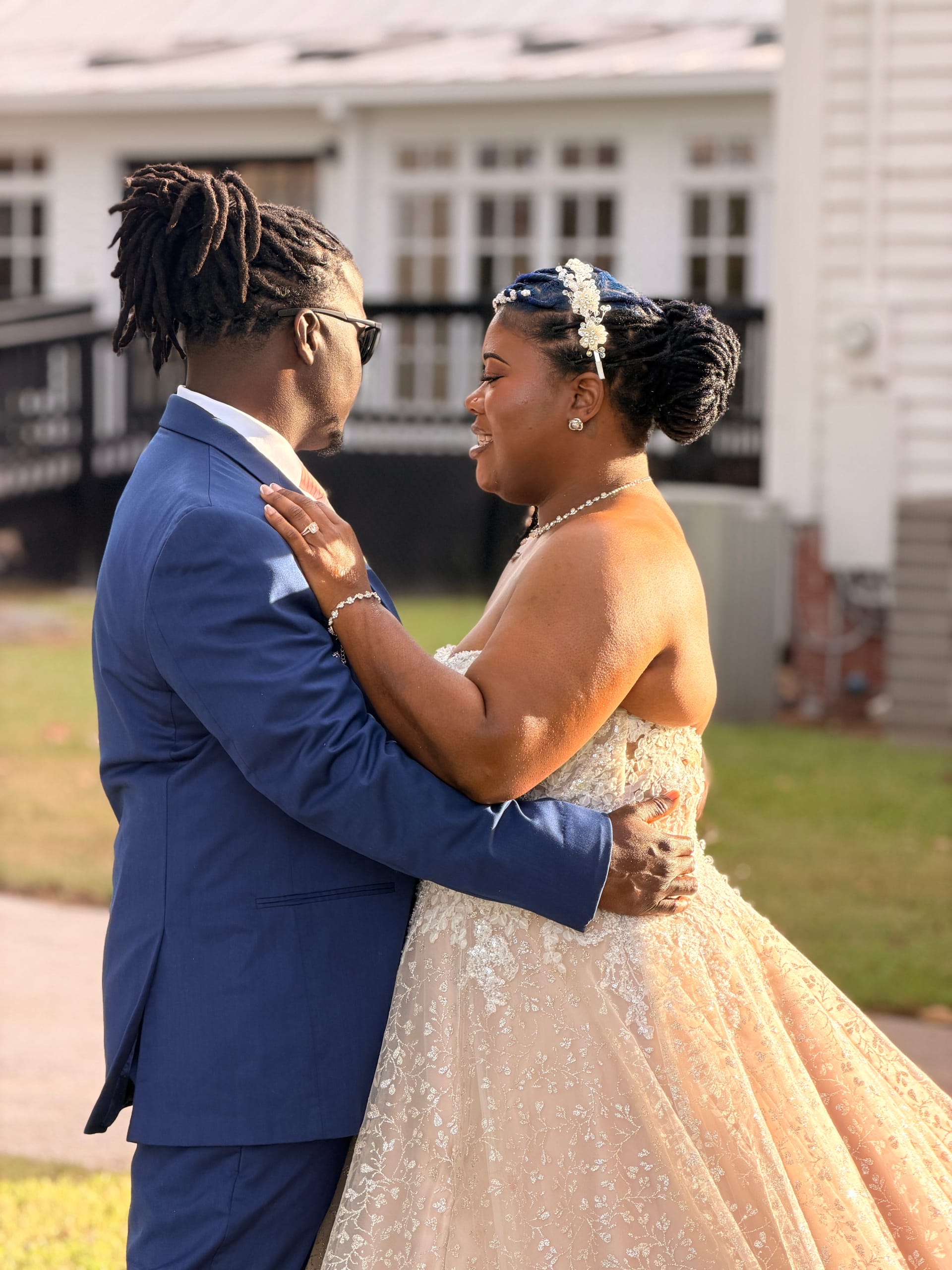A bride in a champagne lace ball gown laughs joyfully as she embraces her groom in a navy suit during a golden-hour first look in front of the historic Scarborough House manor.