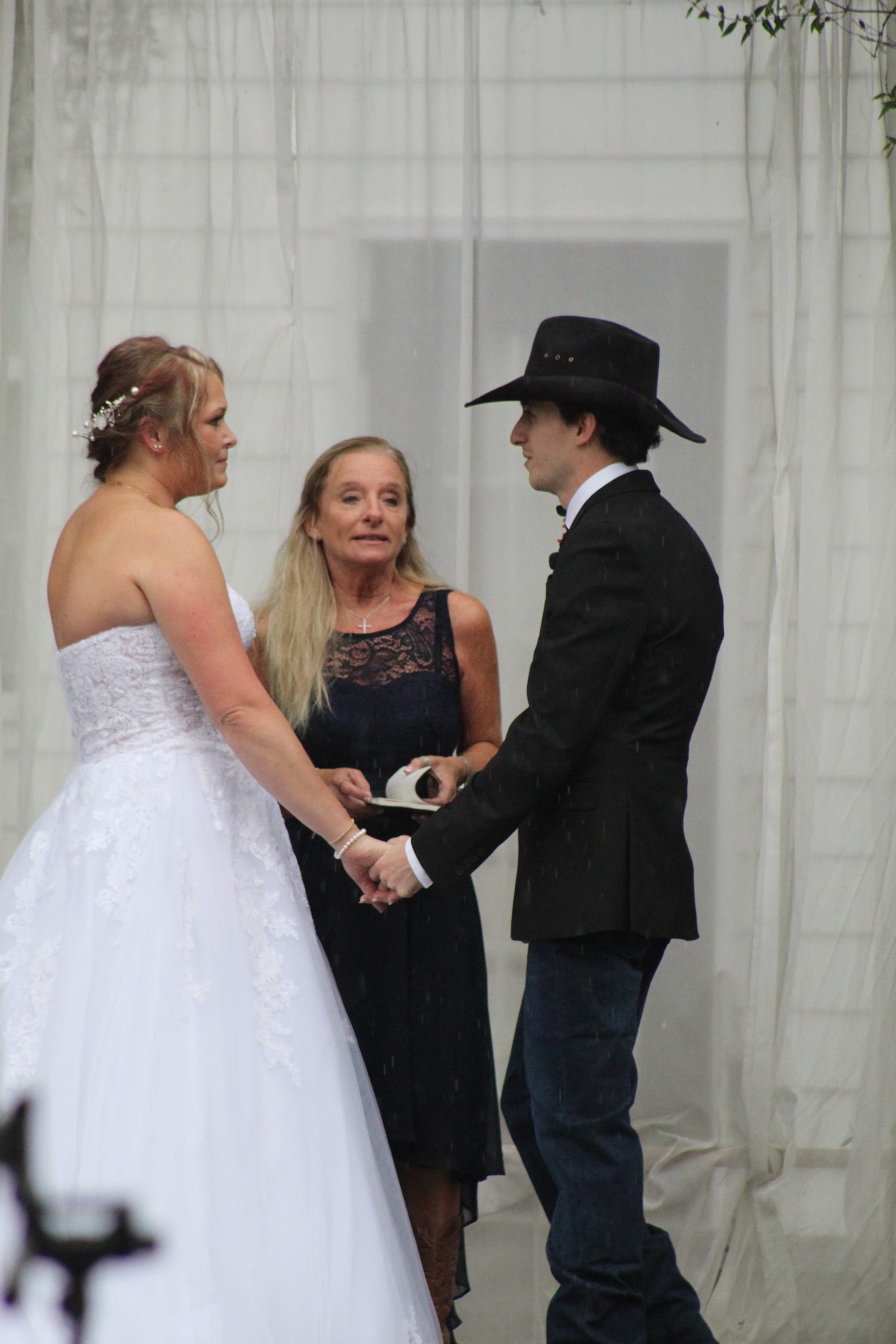 Bride and groom exchange vows while holding hands before an officiant beneath sheer white draping at a historic estate wedding ceremony.