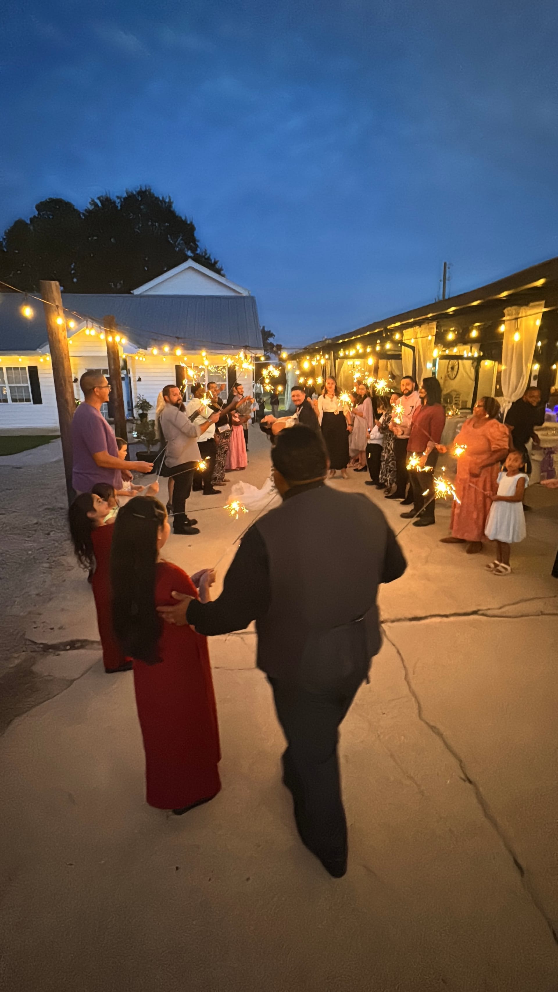 Wedding guests lining a warmly lit outdoor courtyard holding sparklers as the newlyweds walk through during their evening send-off at Scarborough House.