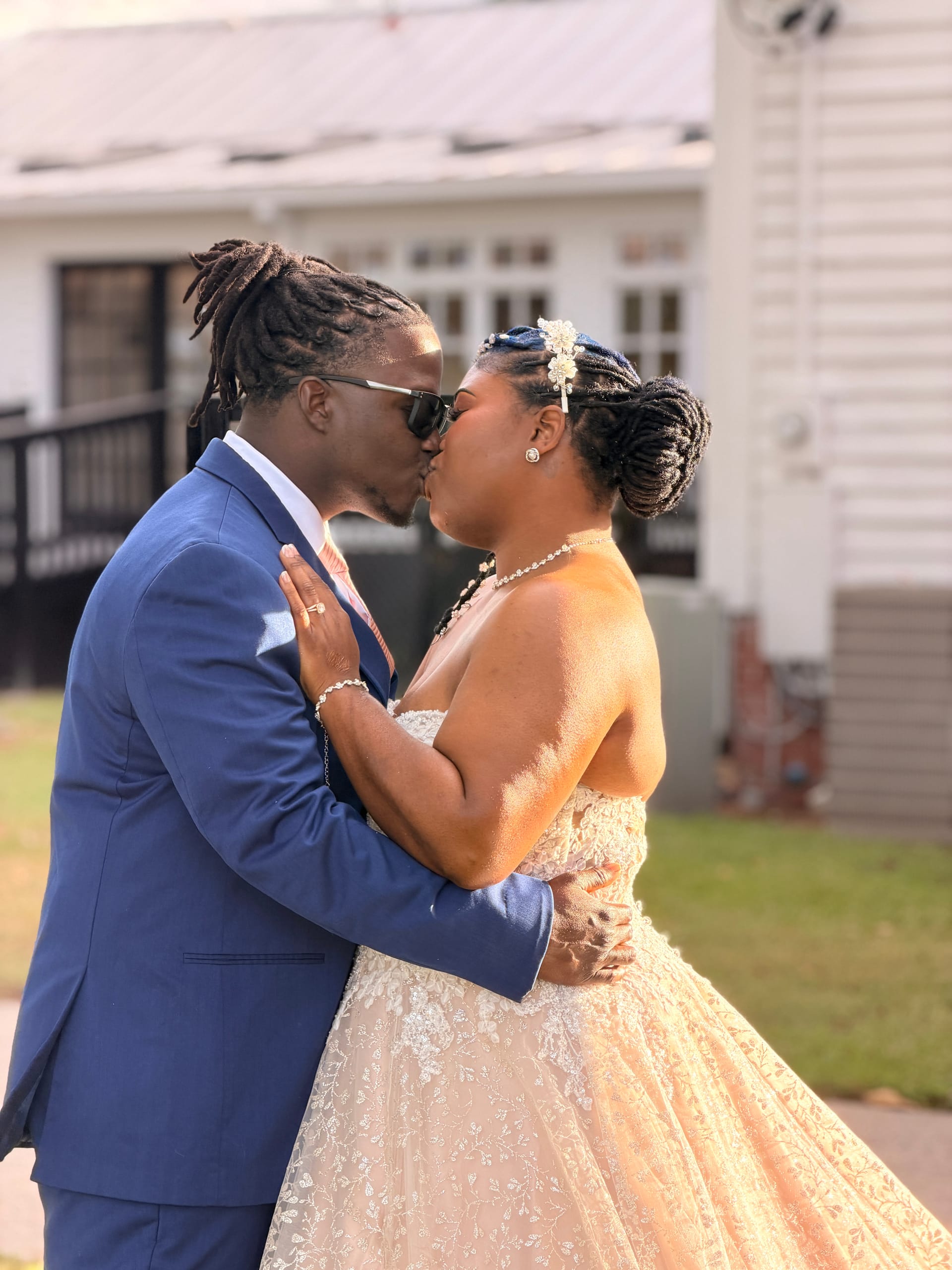 Bride in a champagne lace ballgown and groom in a blue suit share a kiss outside the historic 1821 Scarborough House manor on their wedding day.