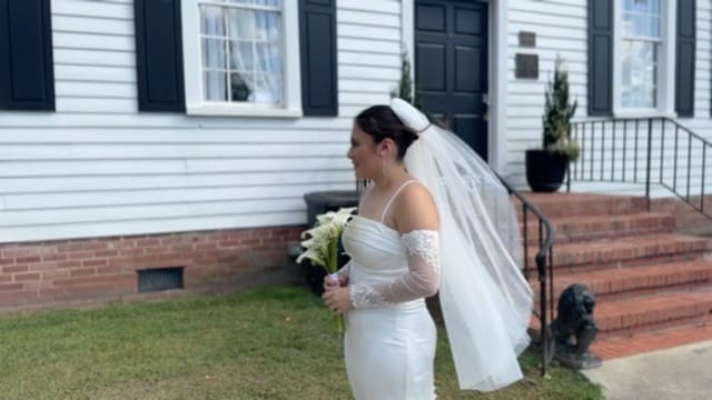 Bride in a fitted white gown and veil holding a white bouquet stands in profile in front of the historic 1821 Scarborough House manor on her wedding day.